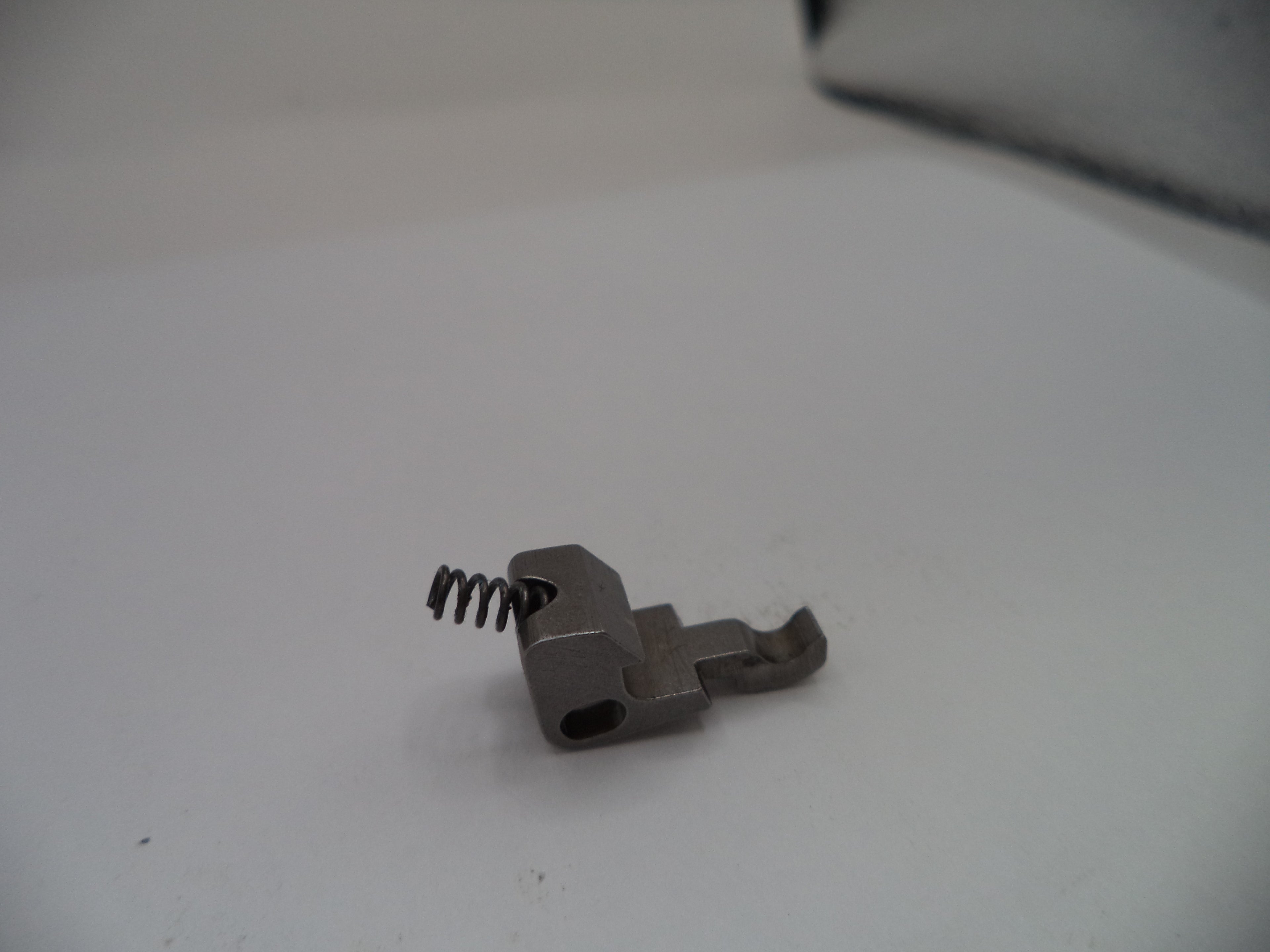Small metal component with a spring on a white surface