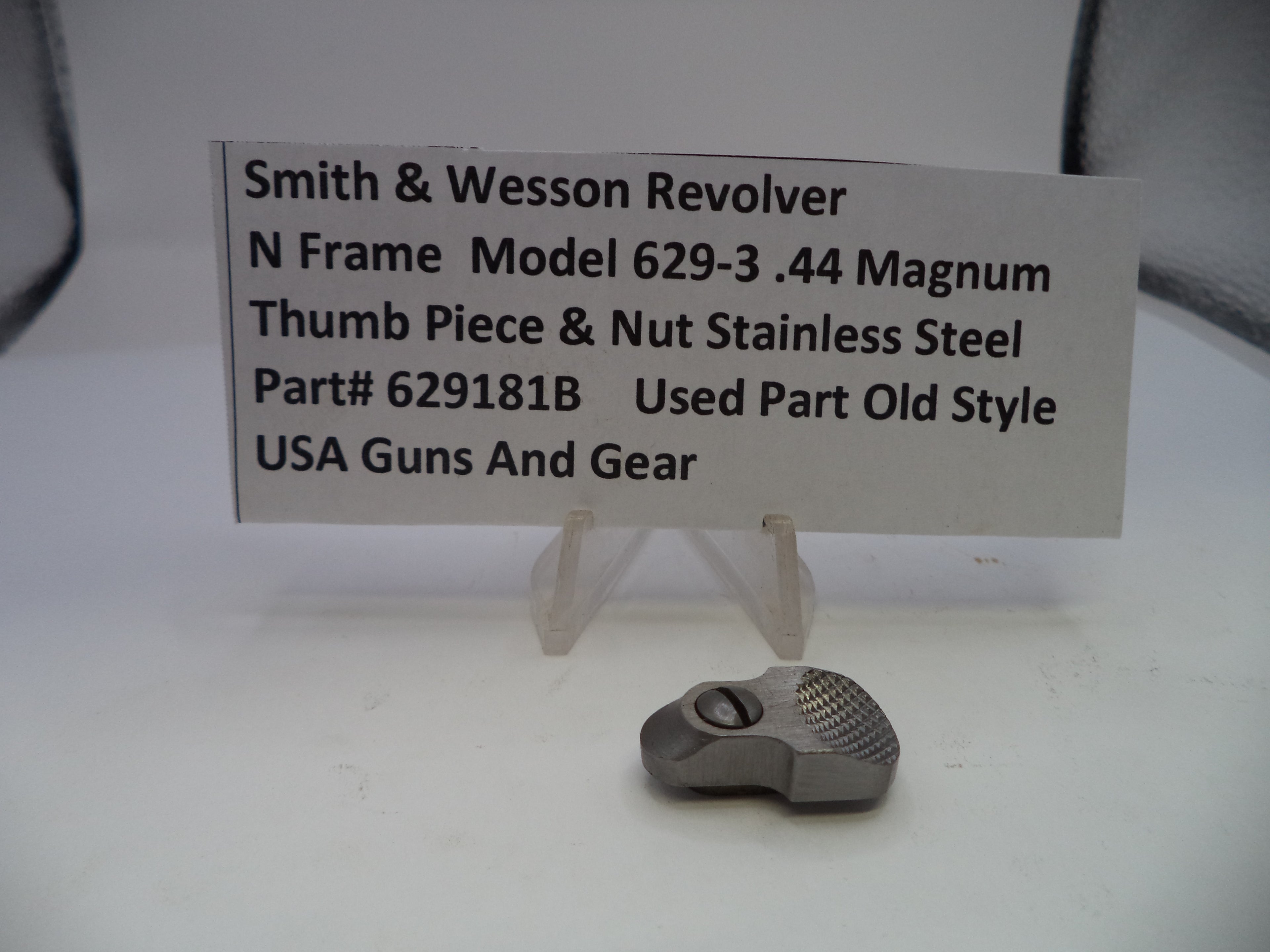 Smith & Wesson revolver thumb piece and nut on a white background with a label.