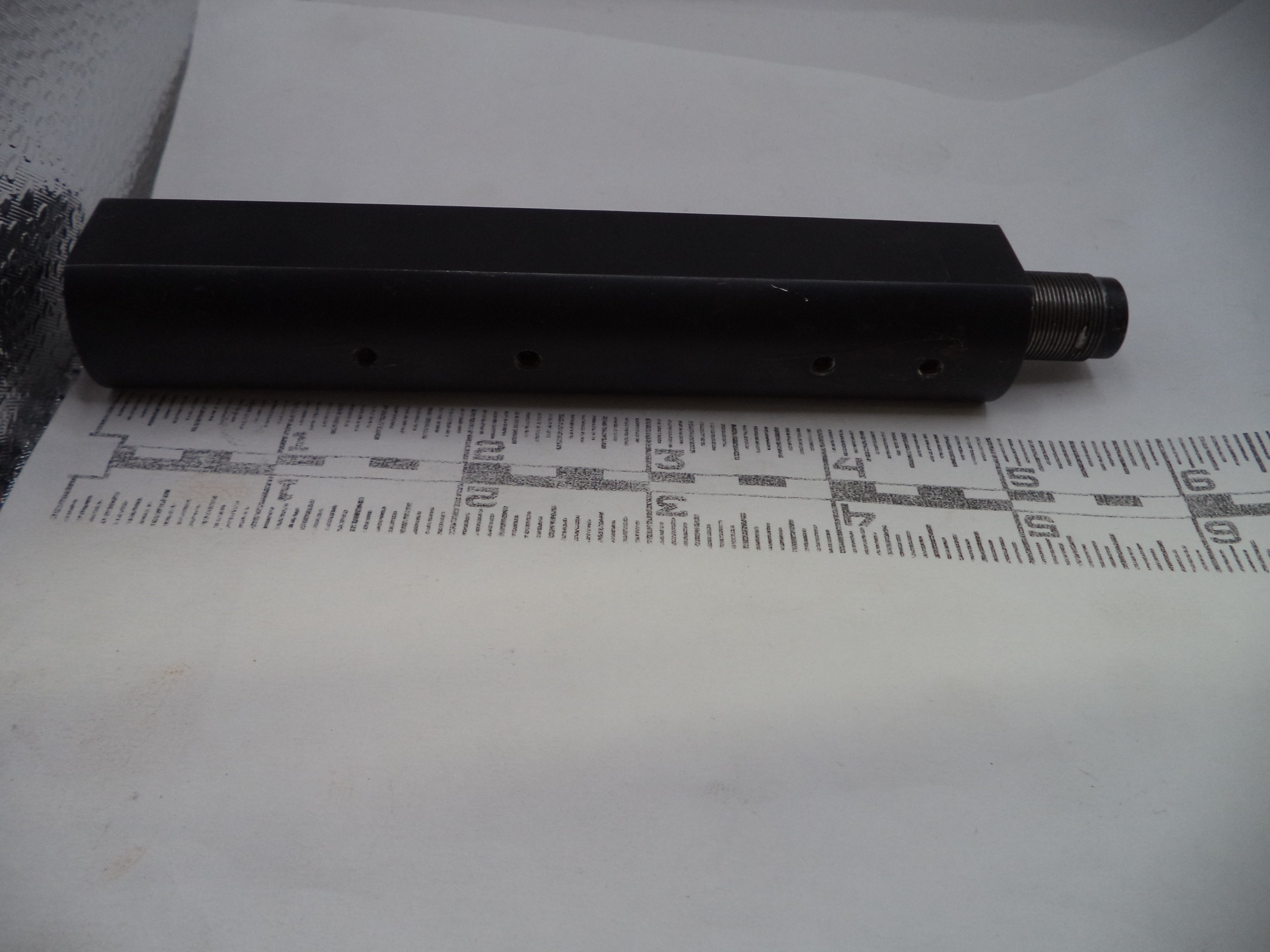 Black cylindrical object on a white surface with a ruler for scale.