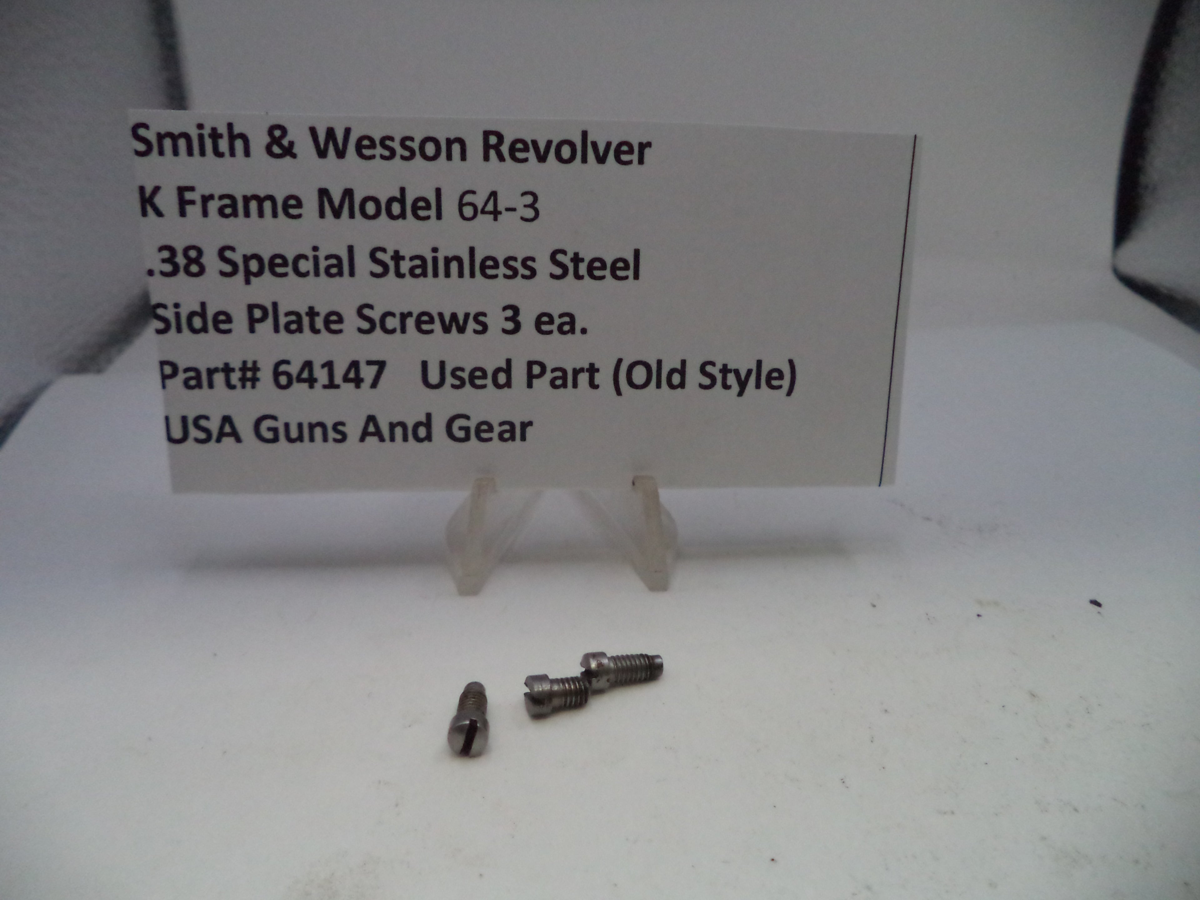 Two small metal screws on a white surface with a label about Smith & Wesson Revolver K Frame Model 64-3 side plate screws.
