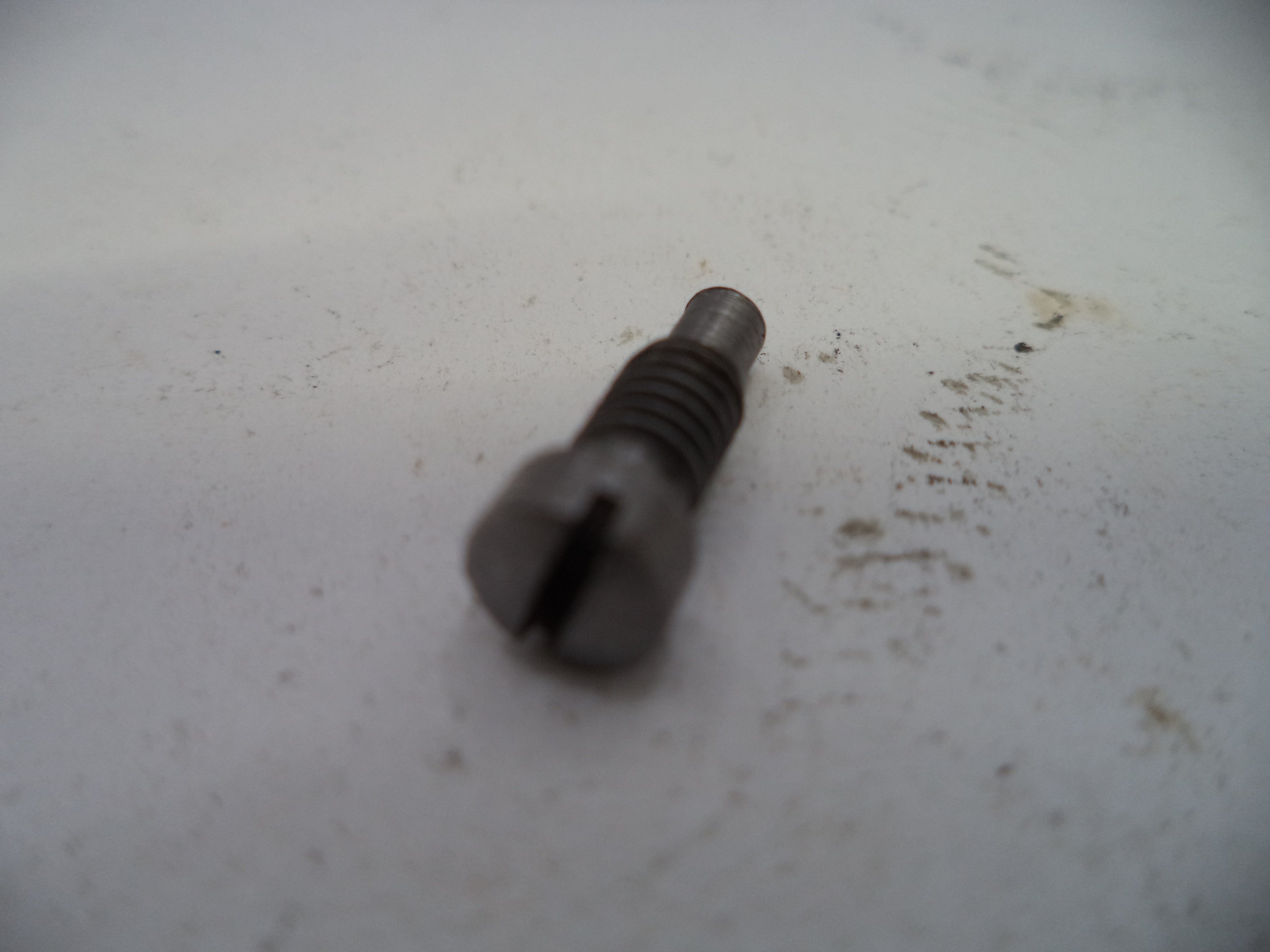 Metal screw on a white surface with visible dirt