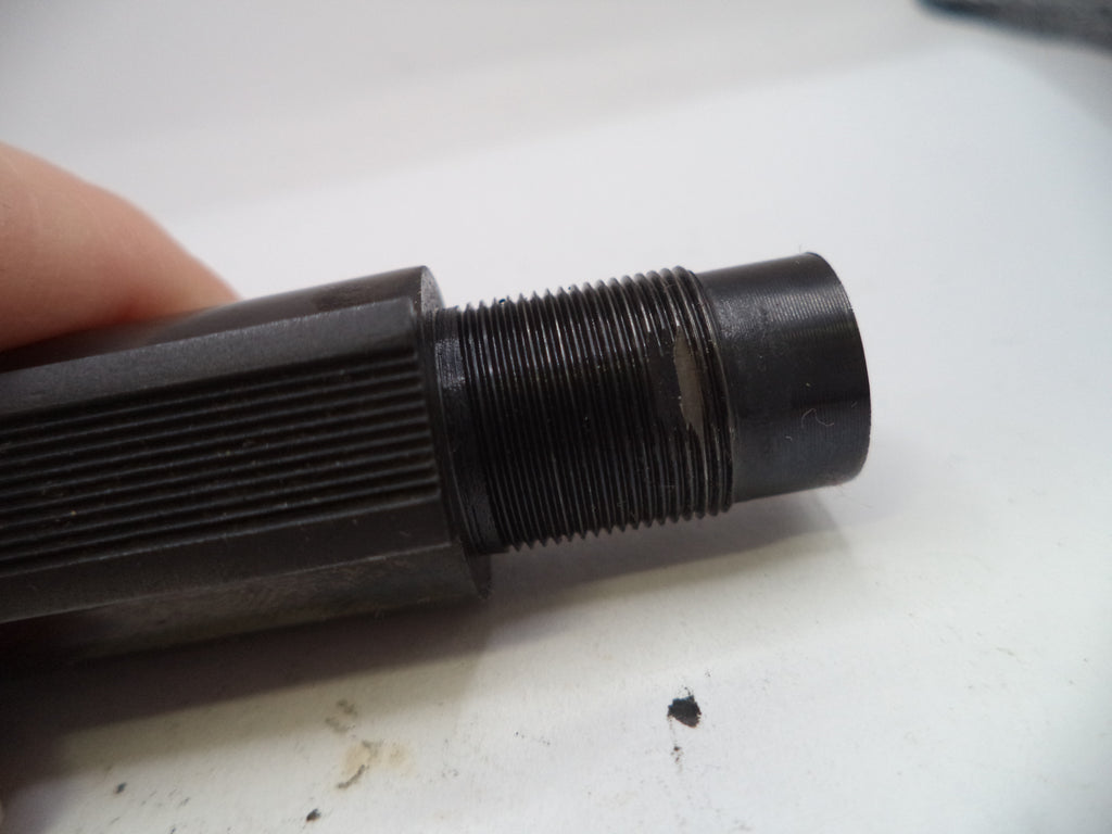 Close-up of a black threaded cylindrical object held by a hand on a white surface.