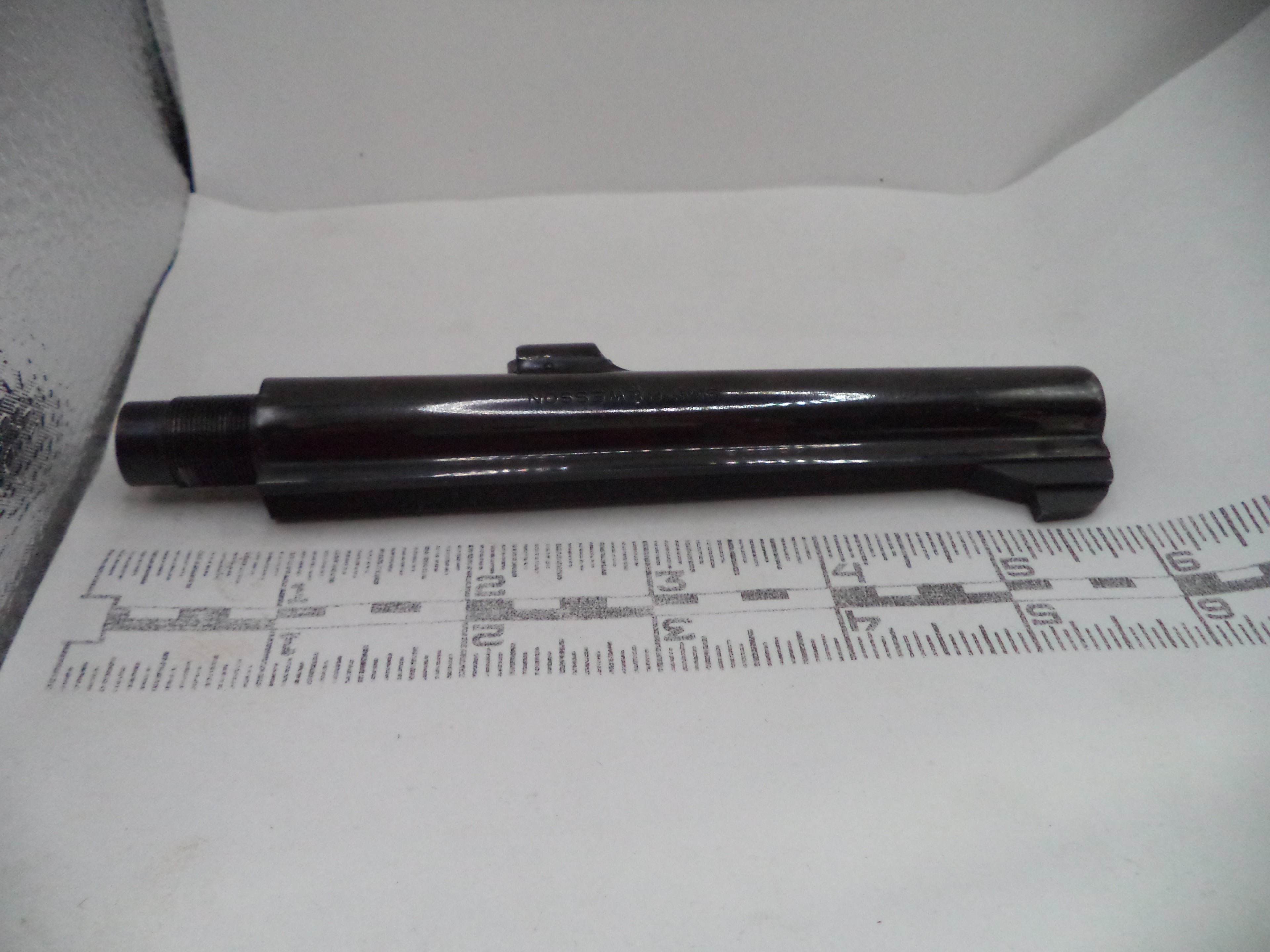 Black cylindrical object on a white surface with a ruler for scale