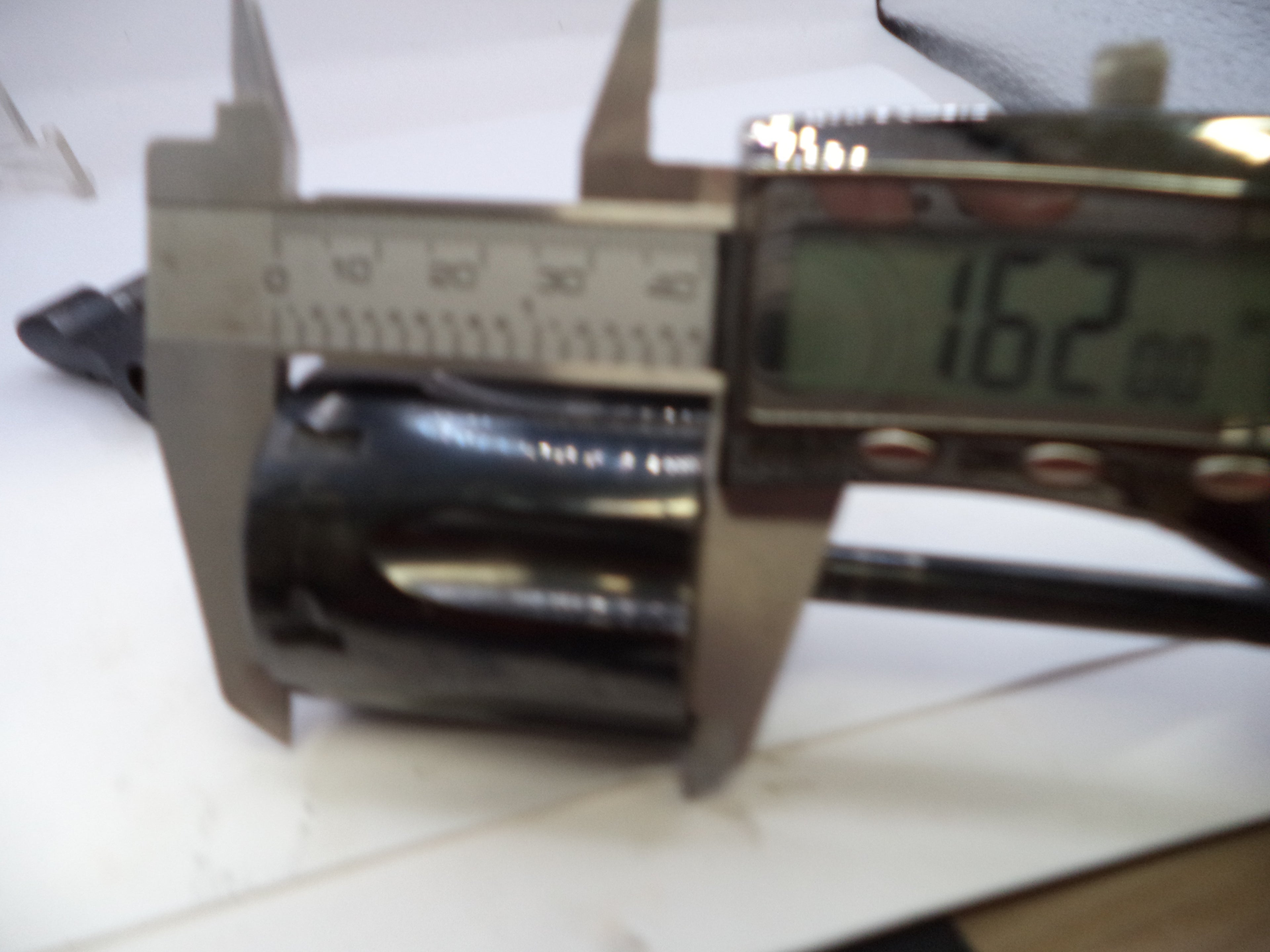 Digital caliper measuring a black metal pipe on a white surface