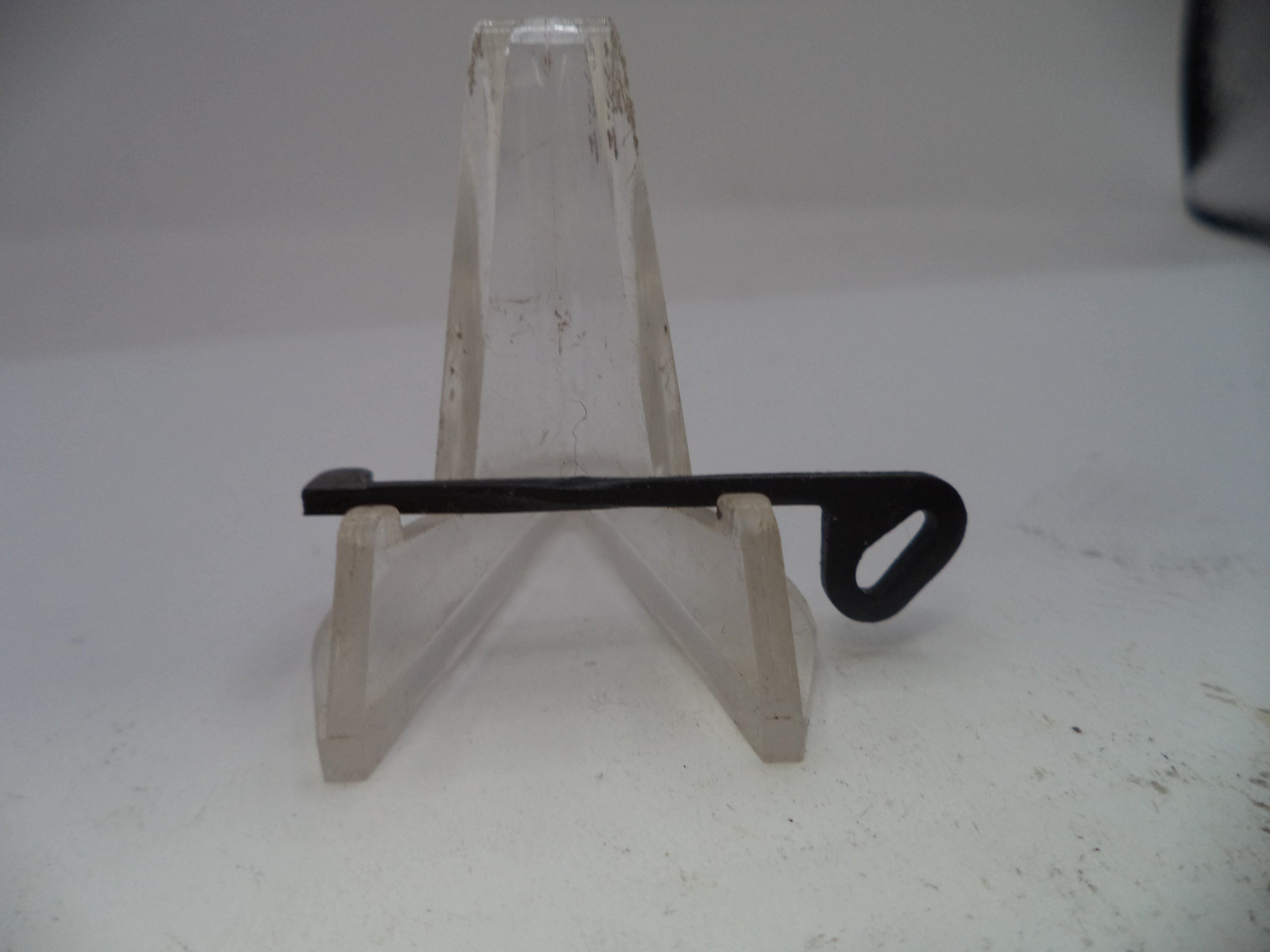 Small black metal tool on a clear acrylic stand against a white background