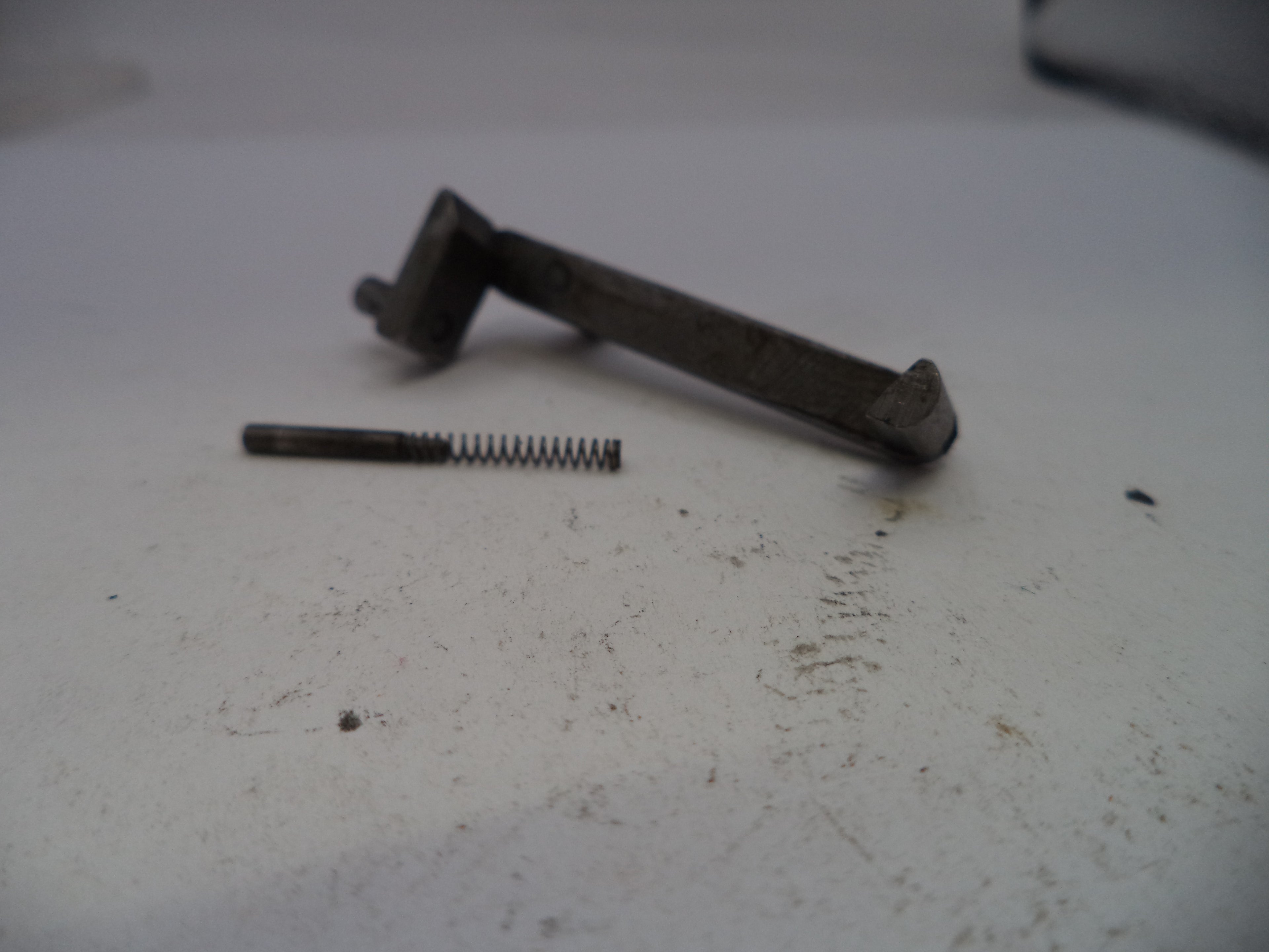 Metal lever and spring on a white surface with visible dirt