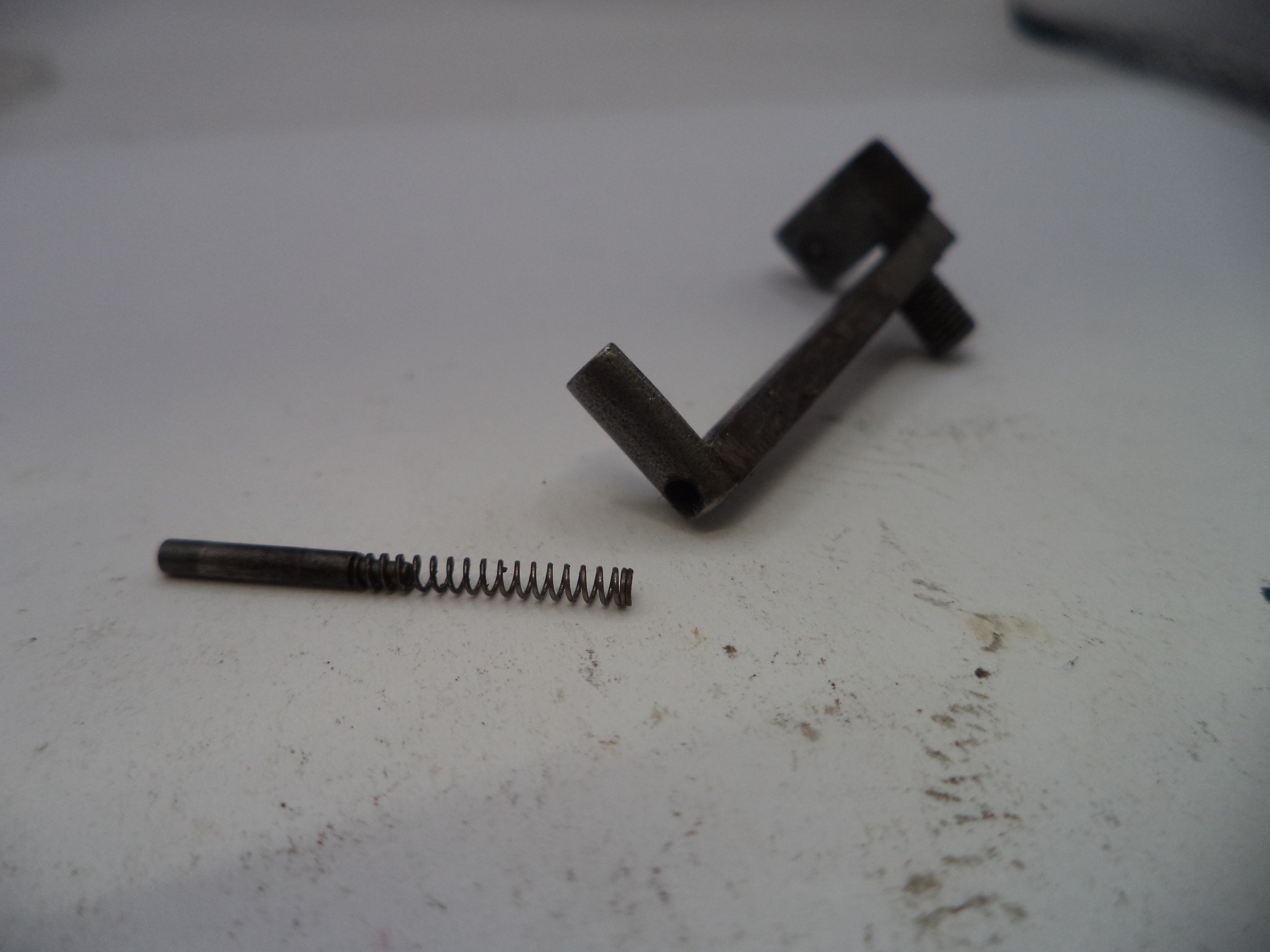 Metal spring and L-shaped bracket on a white surface
