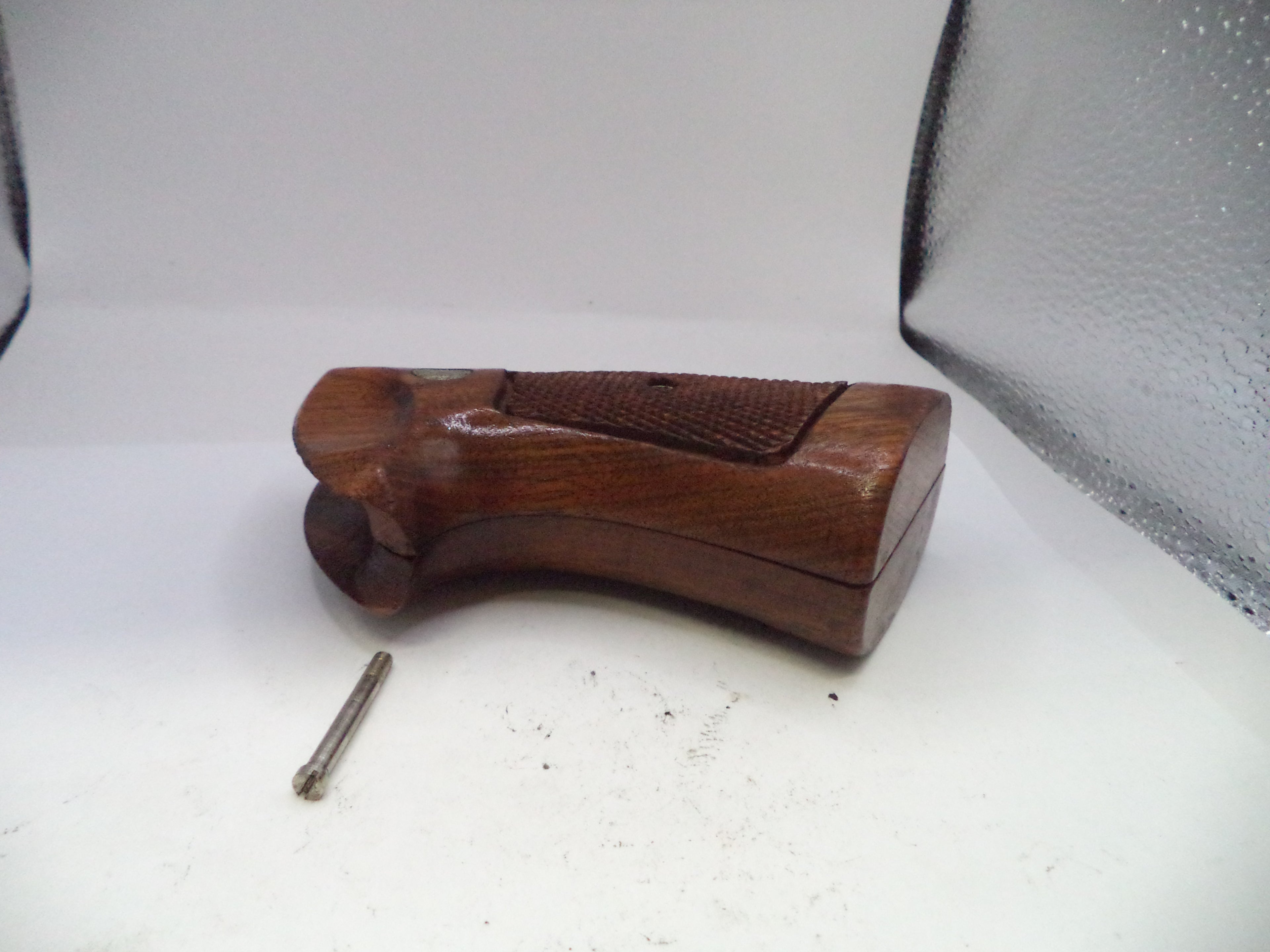 Wooden gun stock on a white surface with a screw beside it