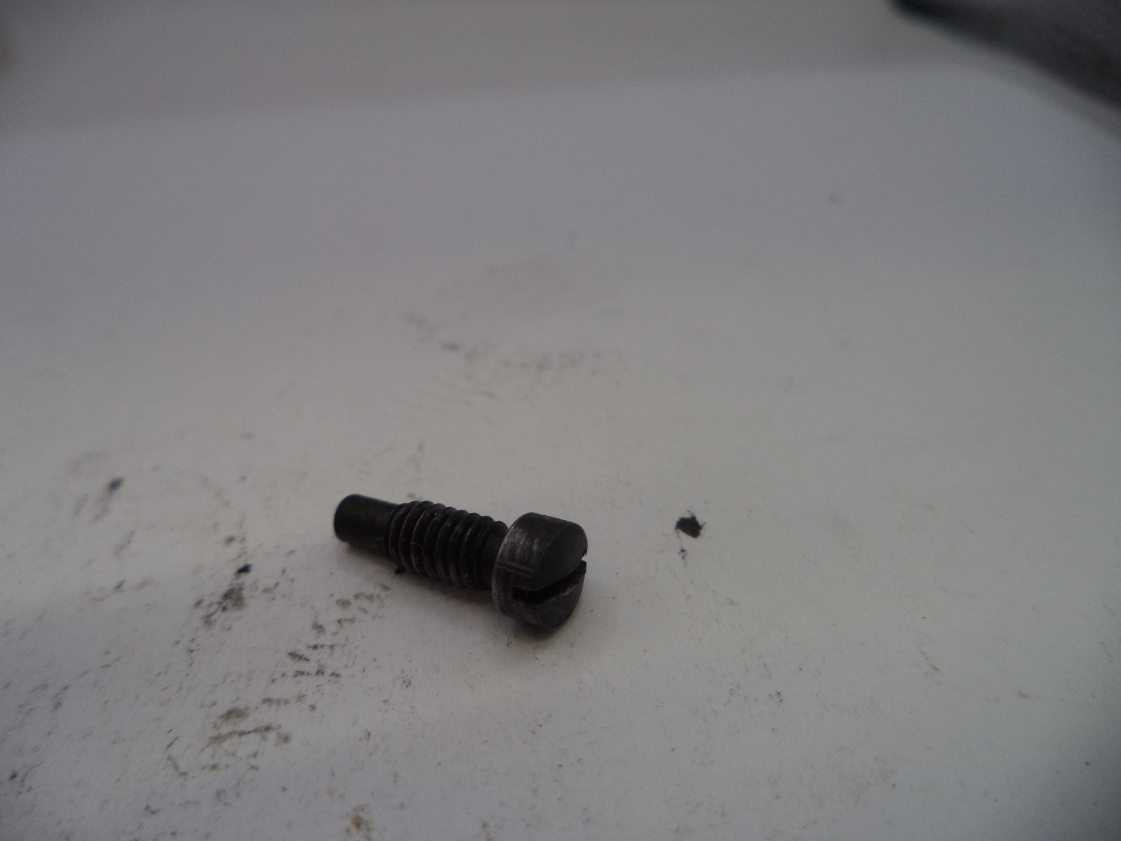 Black screw on a white surface with visible dirt and marks