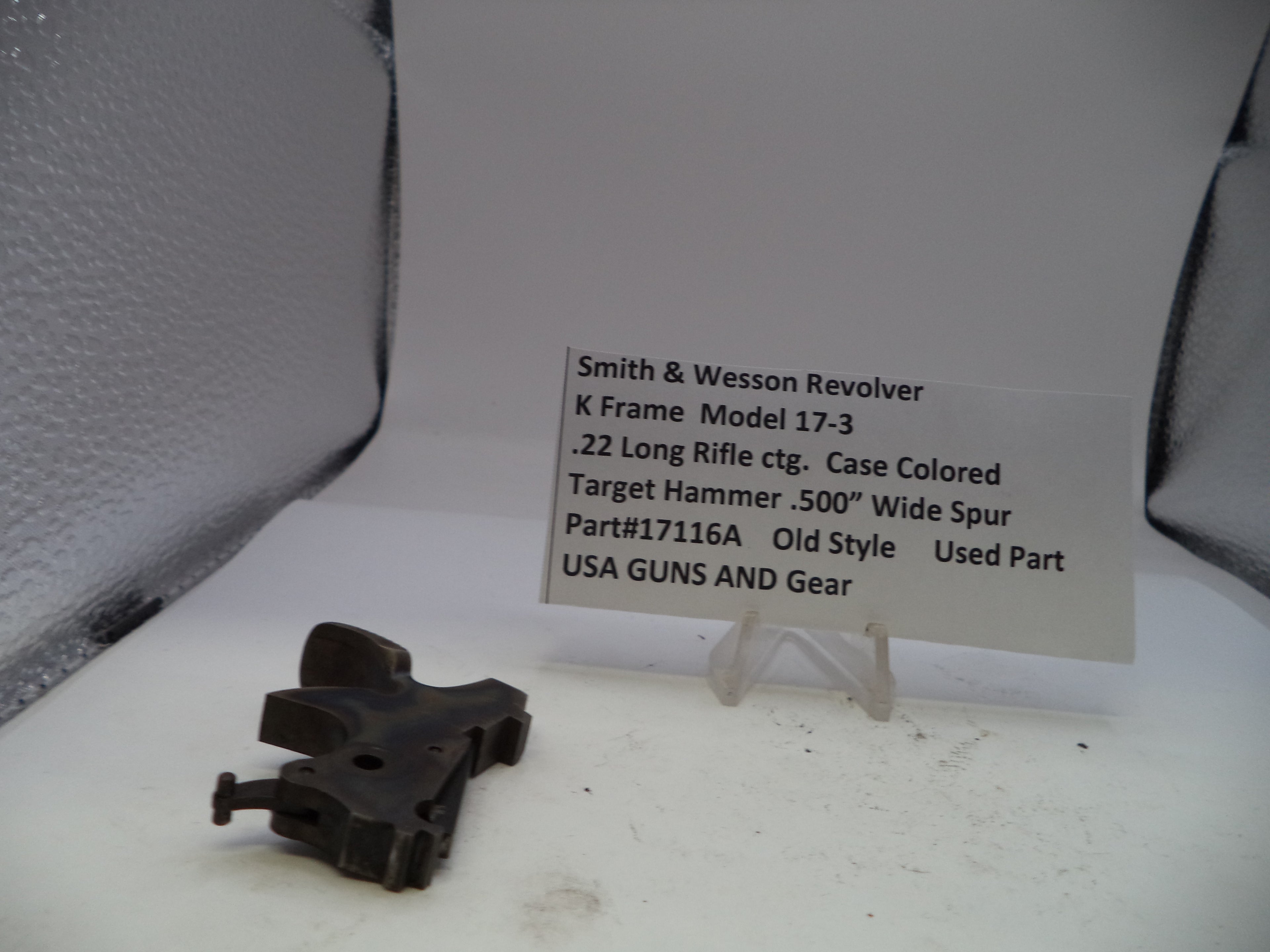 Black gun part on a white surface with a descriptive card in the background