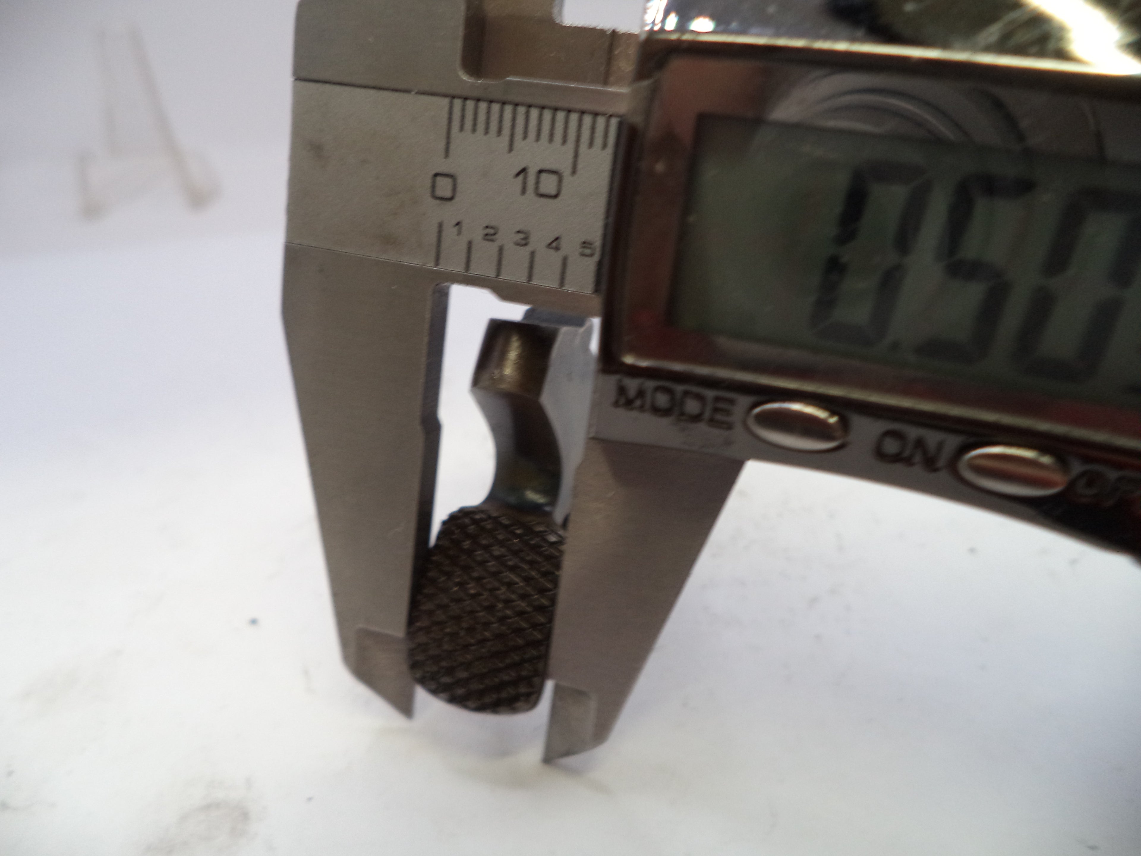 Metallic object being measured with a digital caliper on a white background