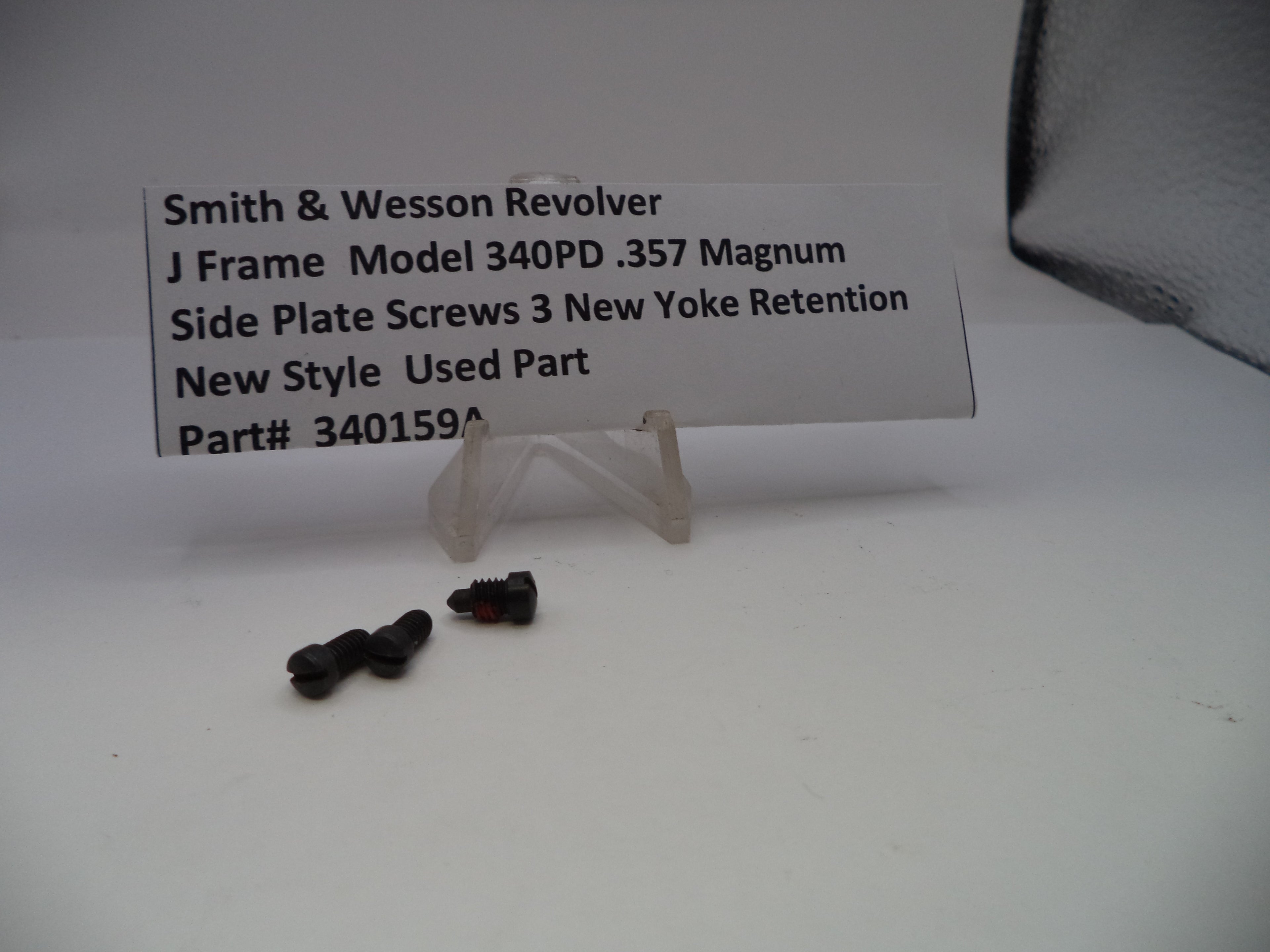 Two screws on a white surface with a label describing a Smith & Wesson revolver part.