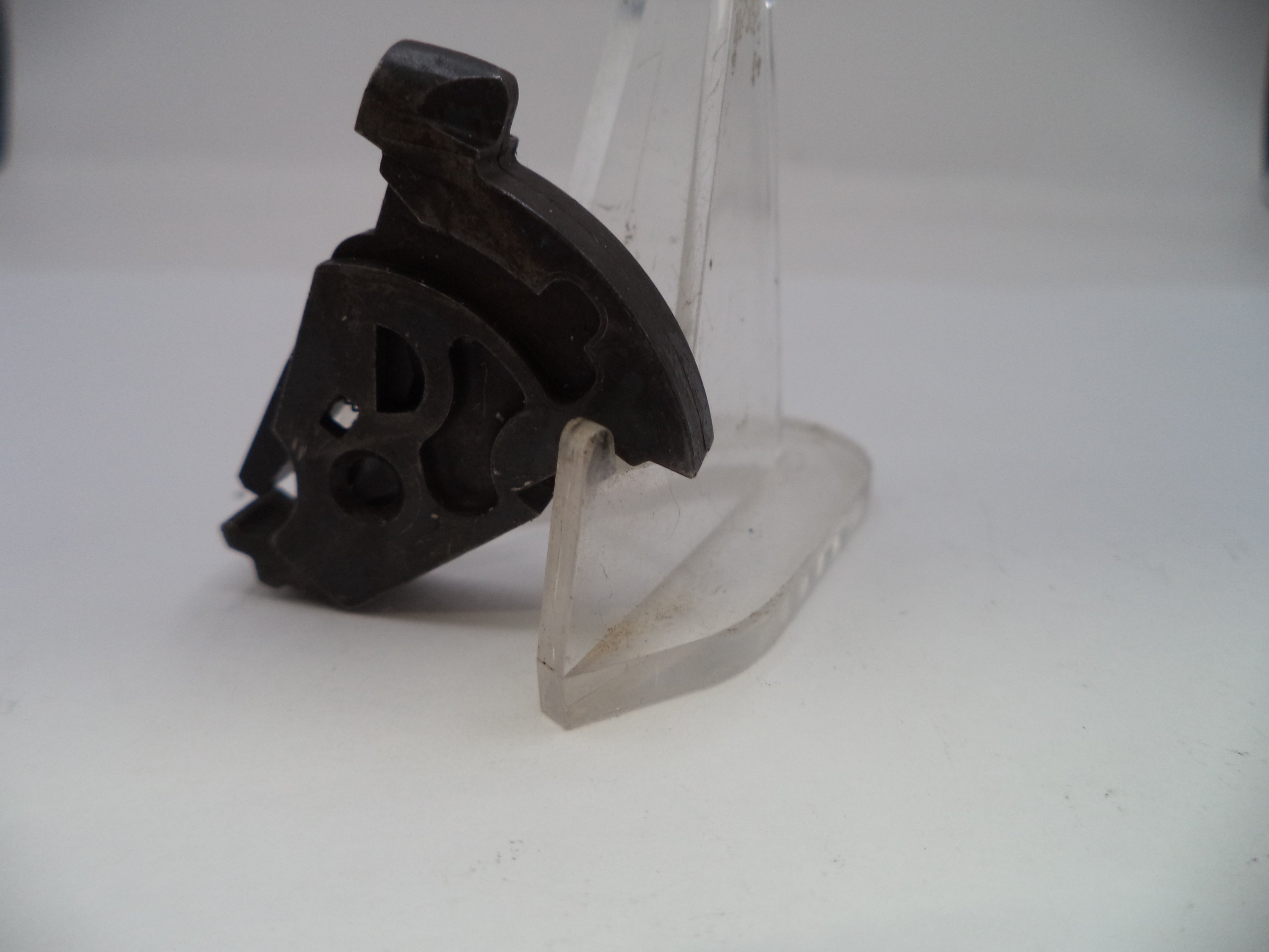 Black plastic component on a clear stand against a white background