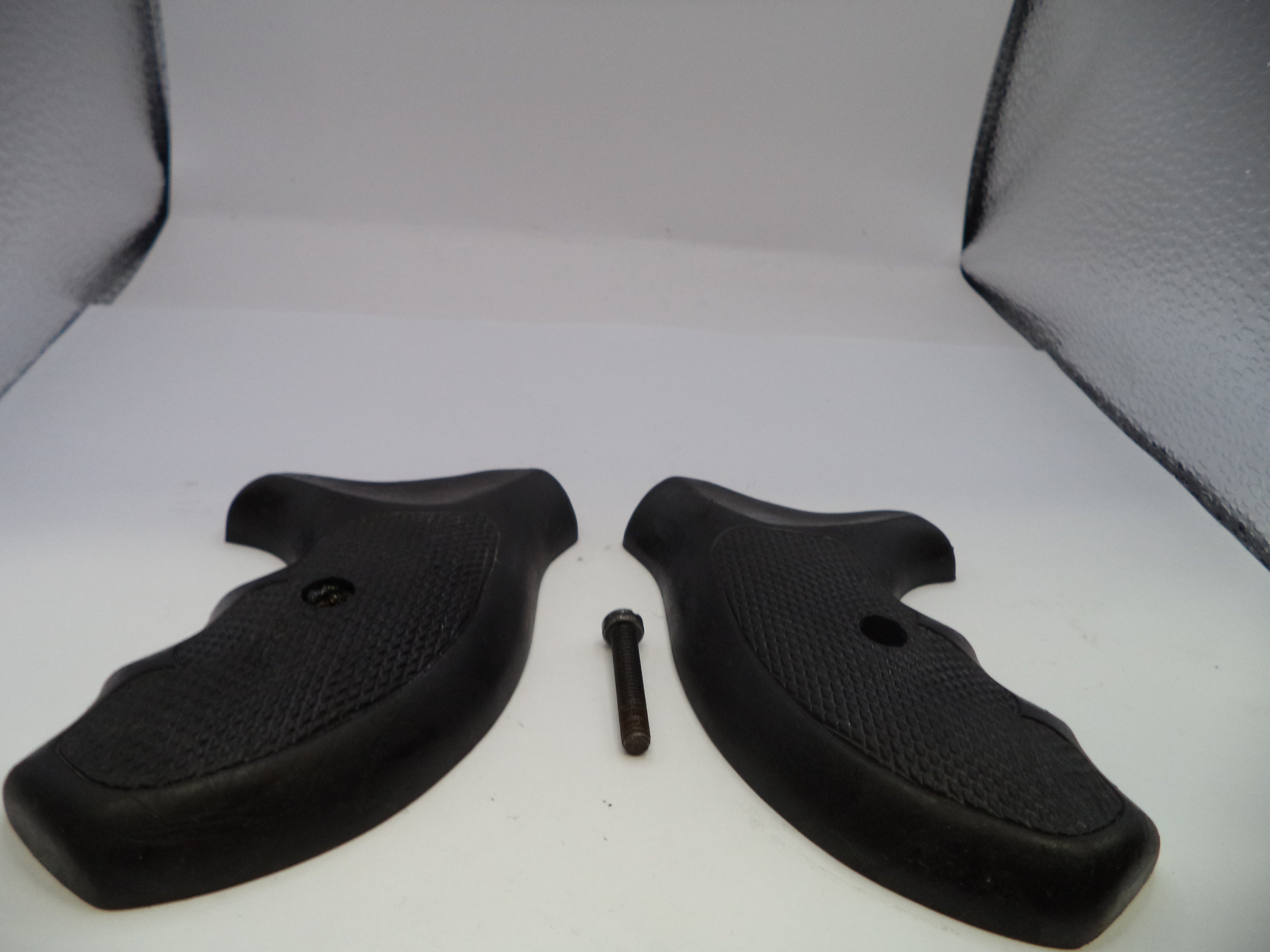 Two black rubber gun grips with a small metal screw on a white surface.