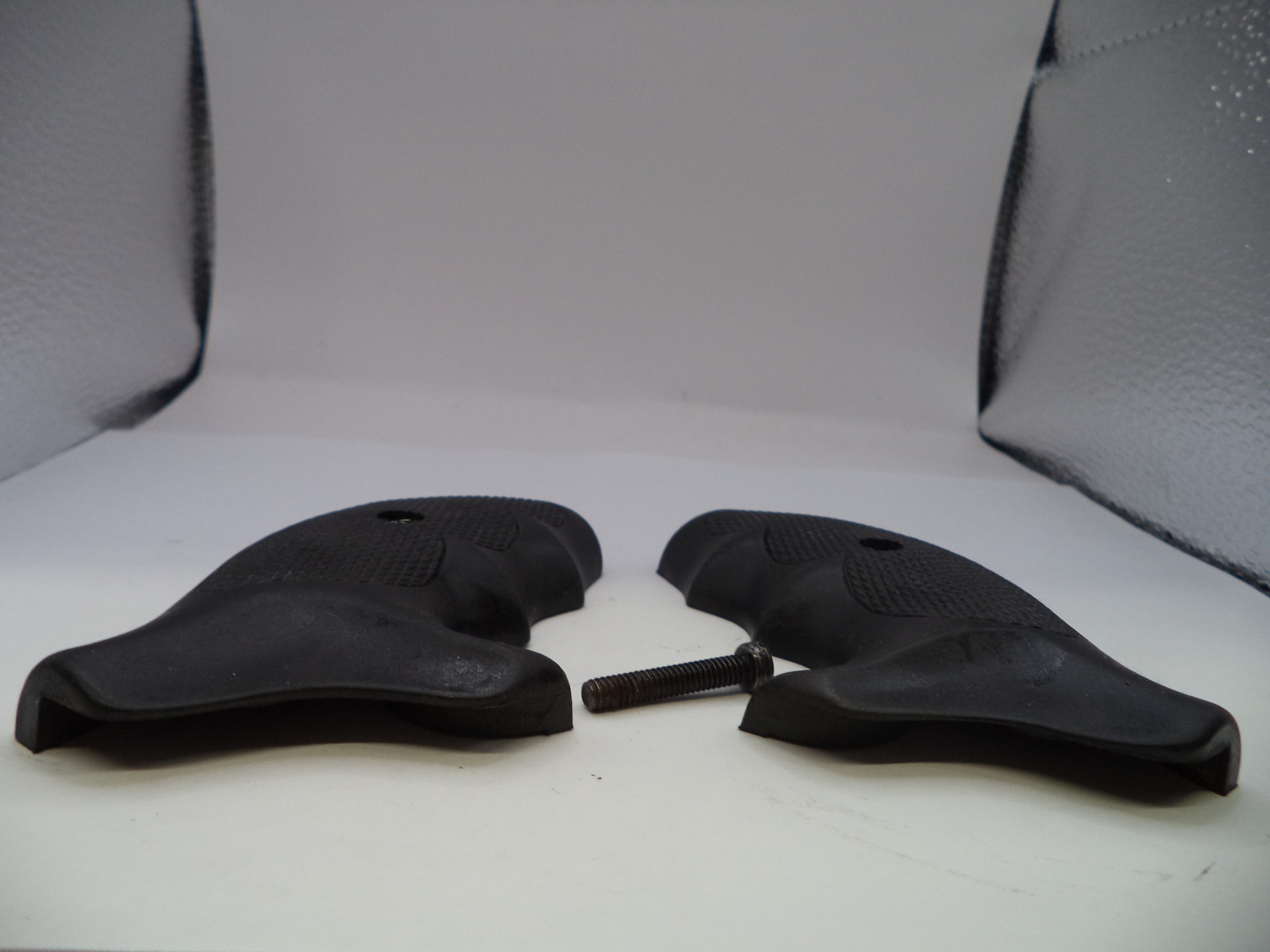 Two black motorcycle seats on a white surface with a gray textured background