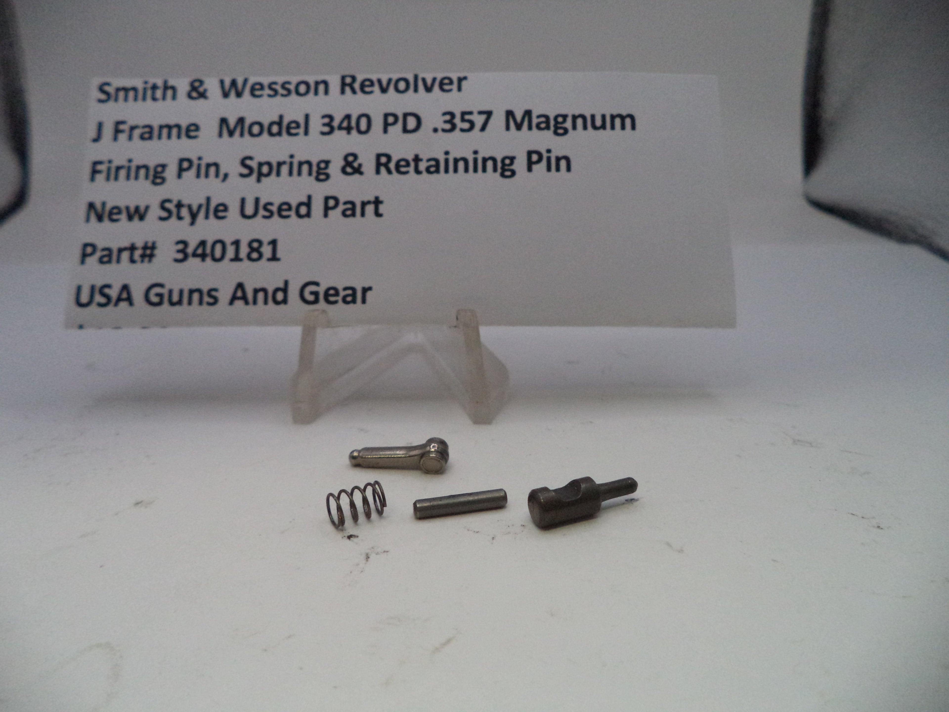 Smith & Wesson revolver parts including a firing pin, spring, and retaining pin on a white surface with a label.