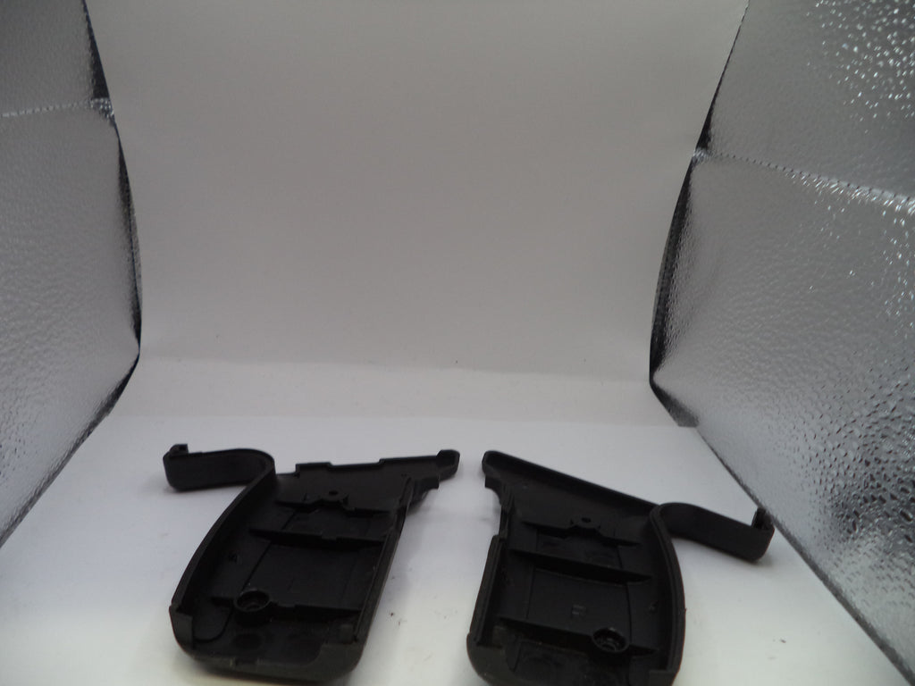 Two black plastic car parts on a white surface with a textured gray background