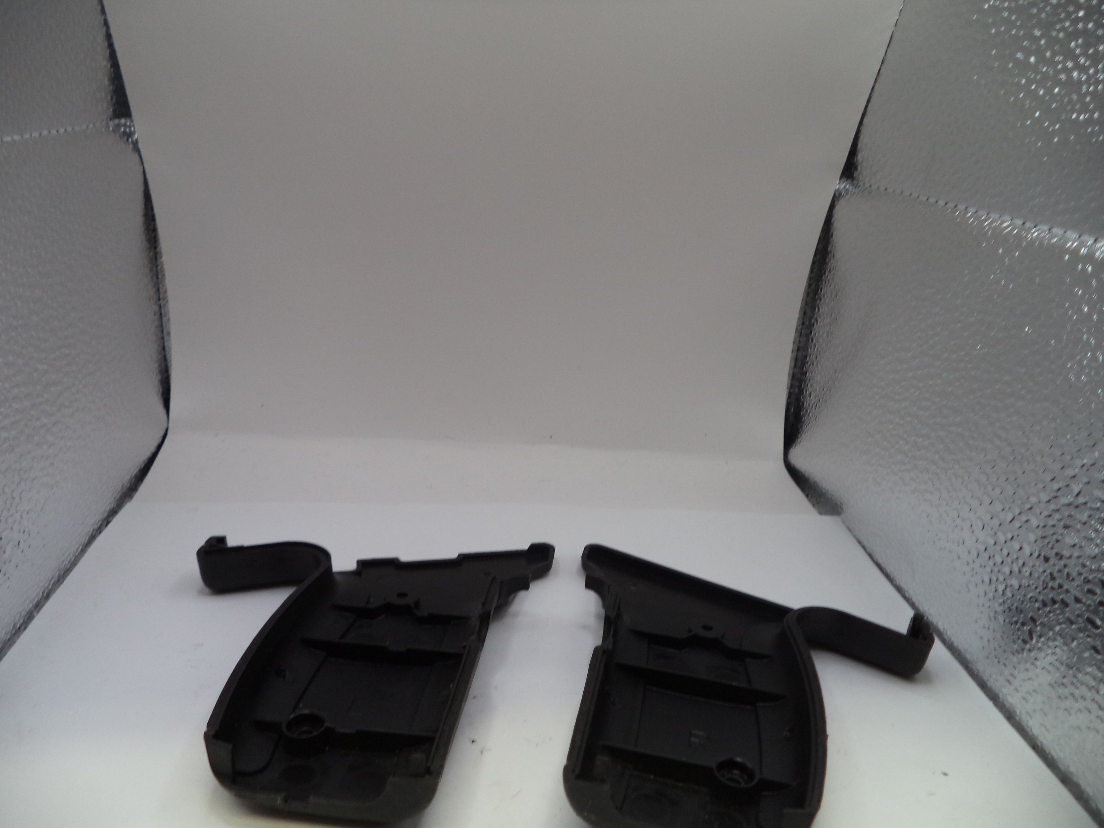 Two black plastic car parts on a white surface with a textured gray background