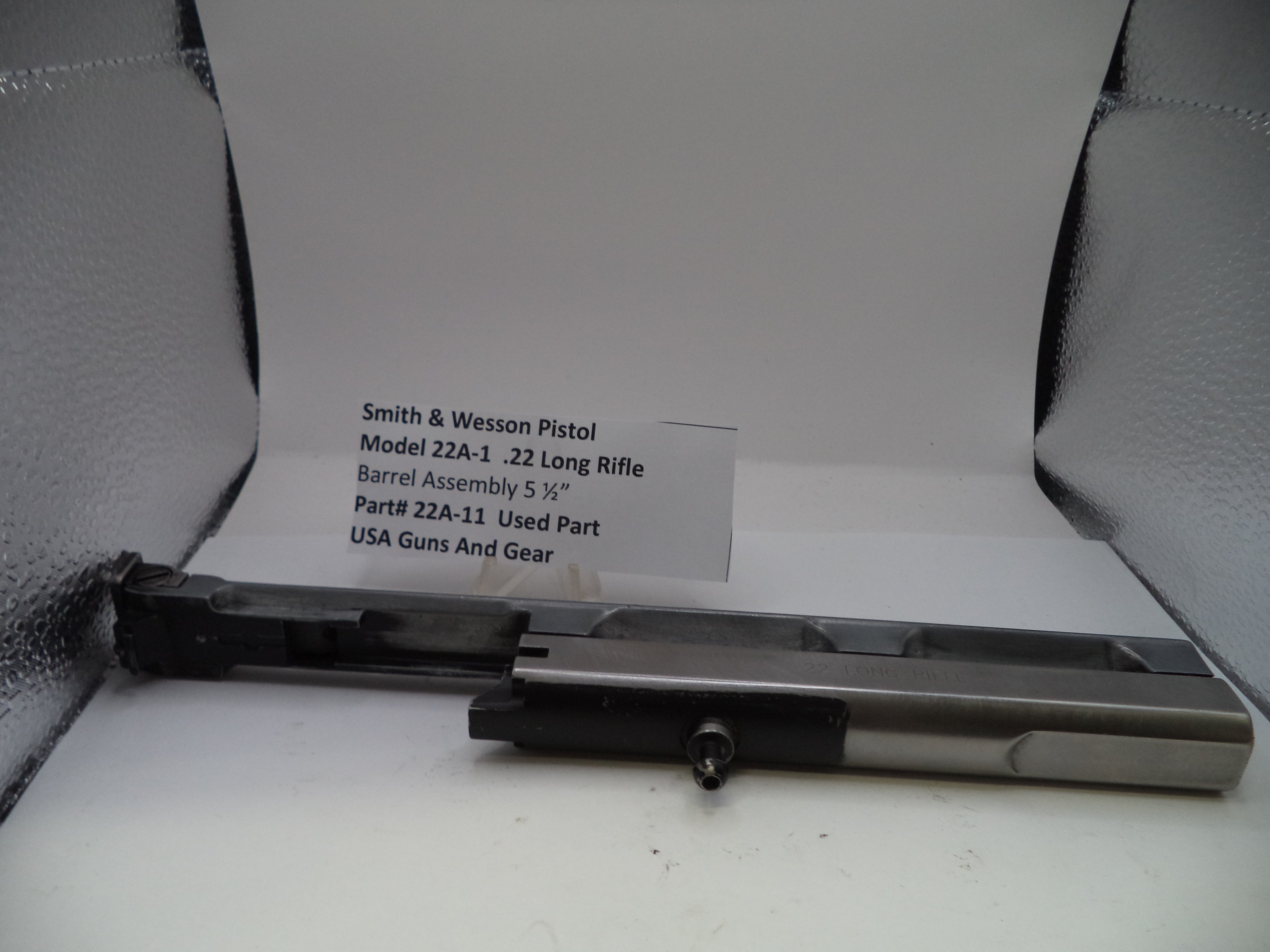 Smith & Wesson pistol barrel assembly on a white surface with a label.