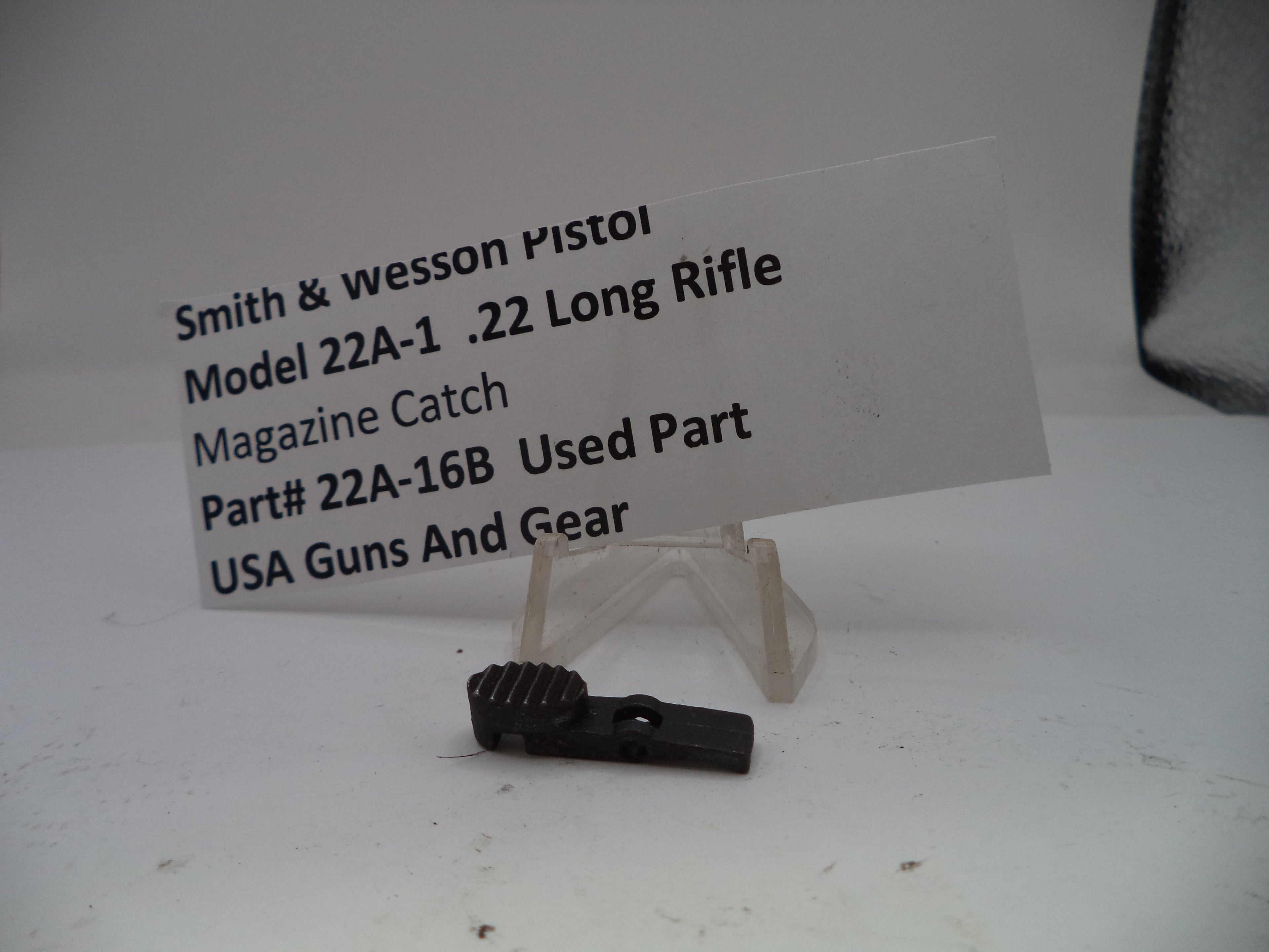 Smith & Wesson pistol magazine catch part with a label on a white background