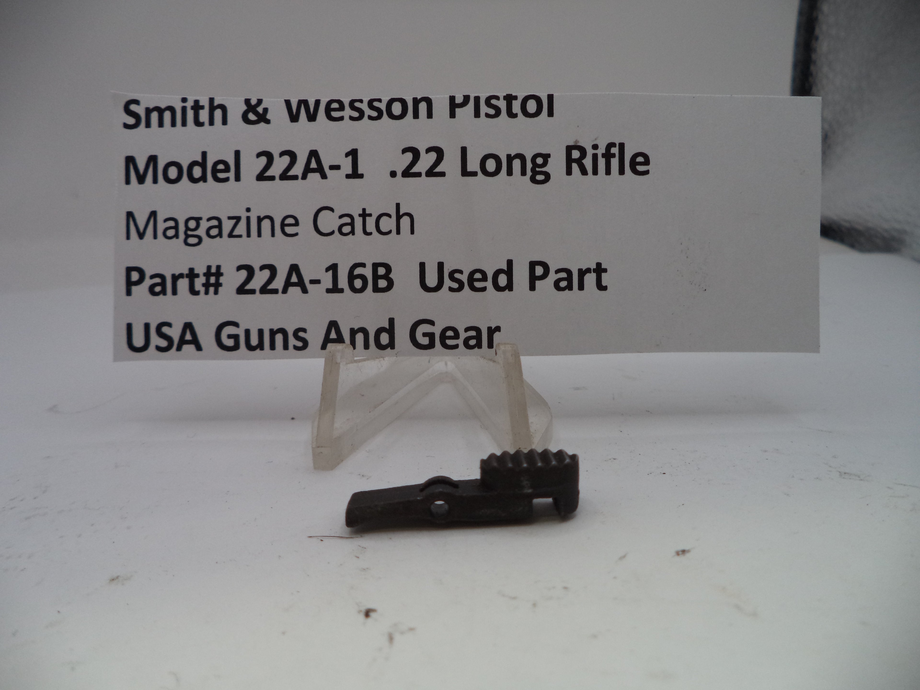 Smith & Wesson pistol magazine catch on a white background with a label.