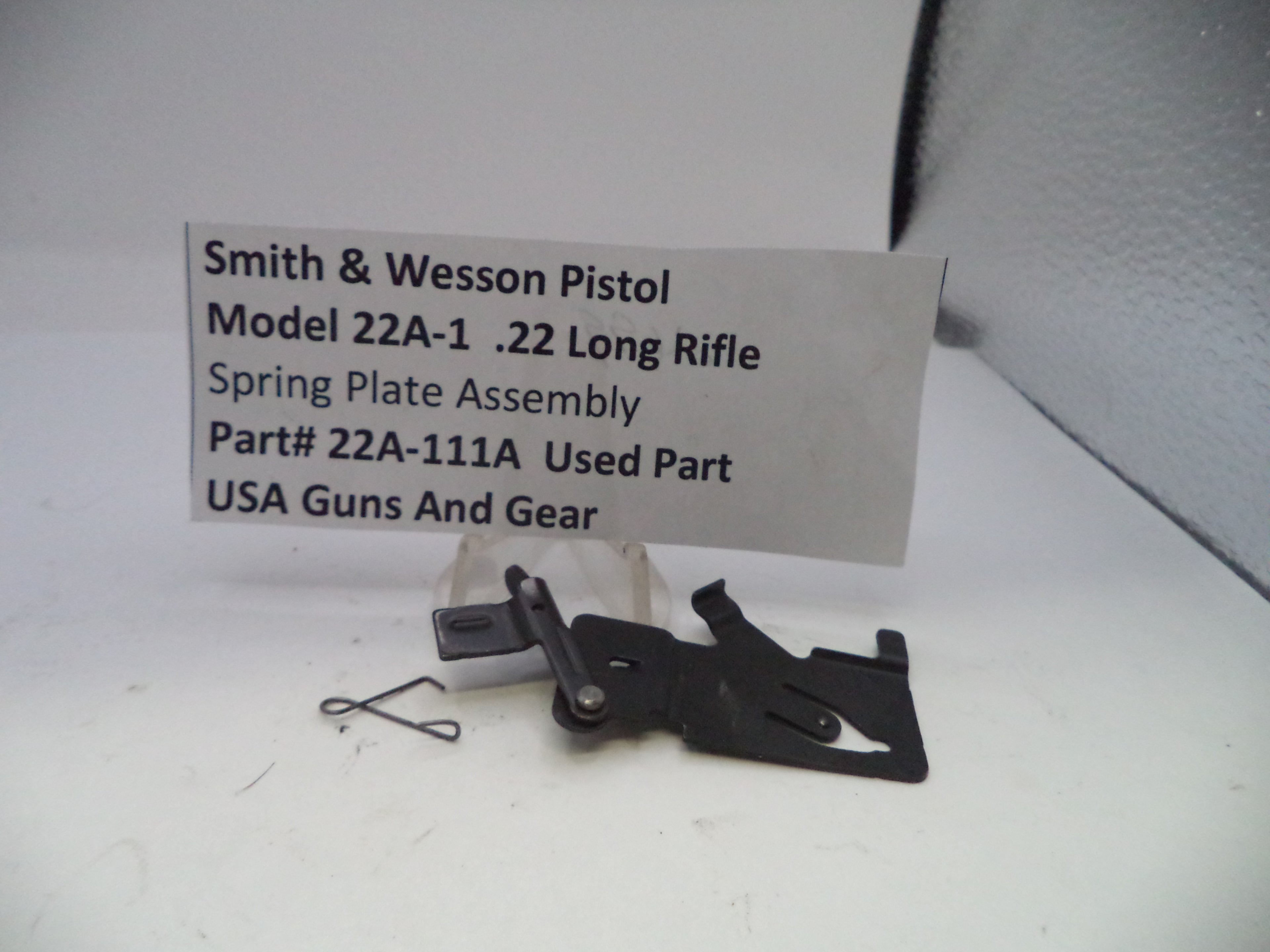Smith & Wesson Pistol Model 22A-1 .22 Long Rifle spring plate assembly on a white surface with a label.