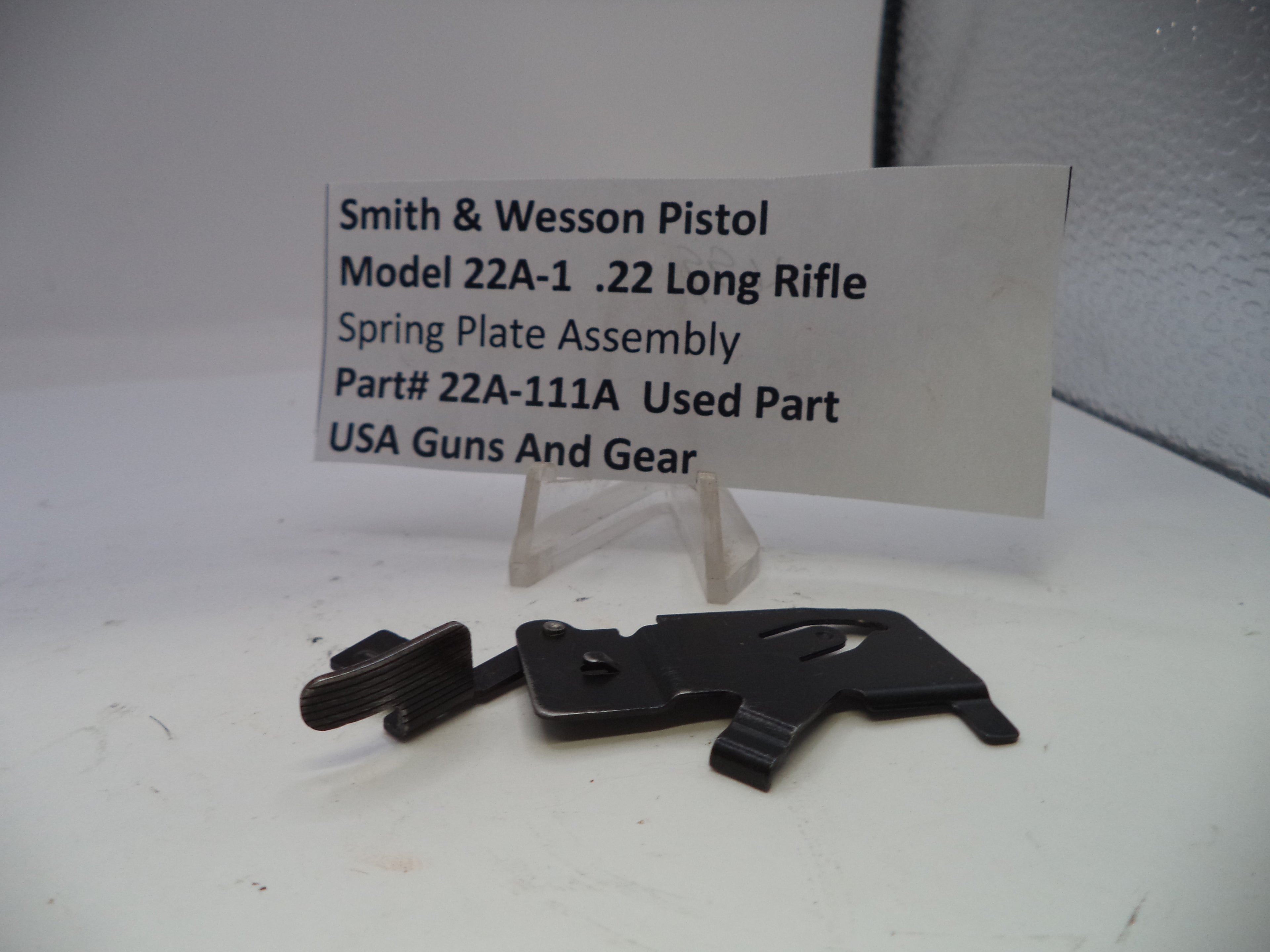 Black spring plate assembly for Smith & Wesson Pistol Model 22A-1 .22 Long Rifle on a white background with a label.