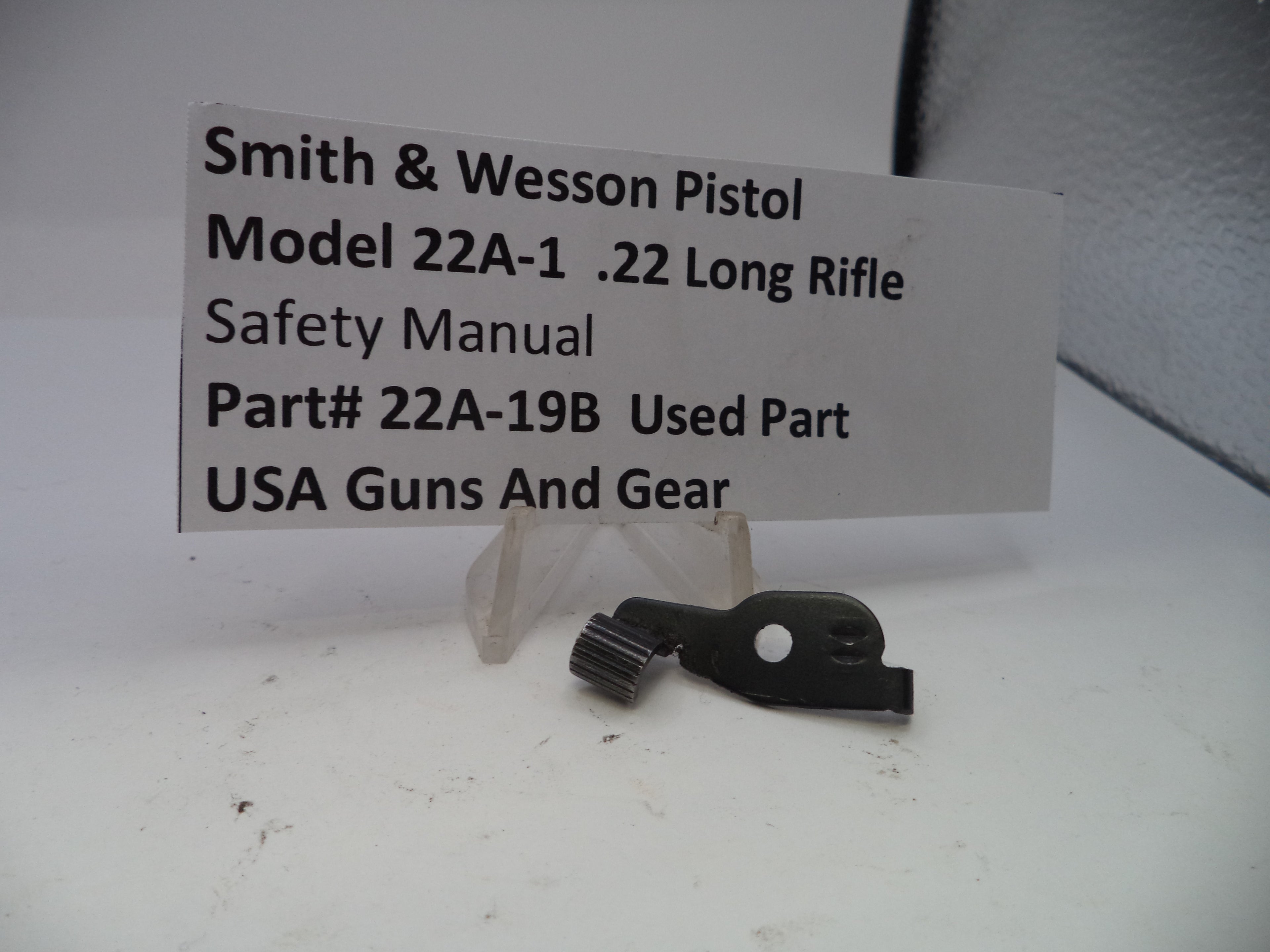 Black safety manual part for Smith & Wesson Pistol Model 22A-1 .22 Long Rifle on a white background with a label.