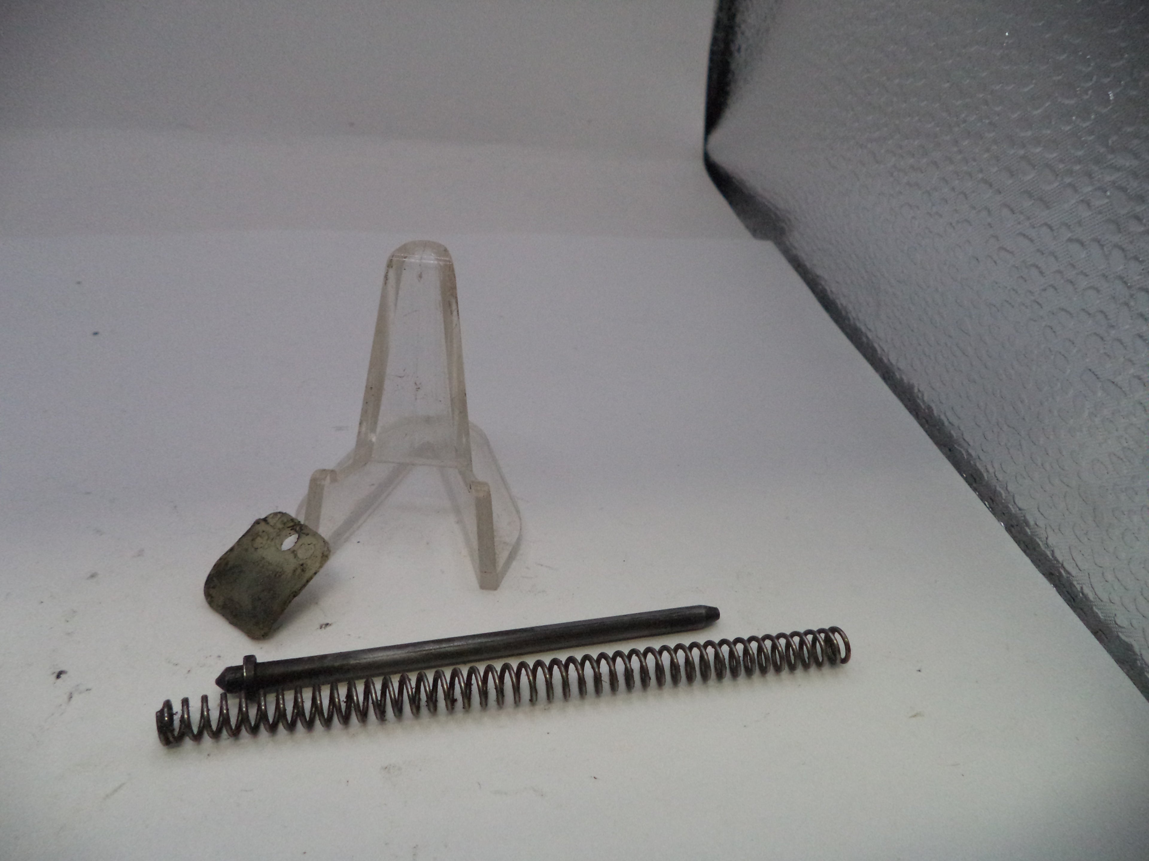 Metal spring and small cylindrical object on a white surface with a clear plastic stand.