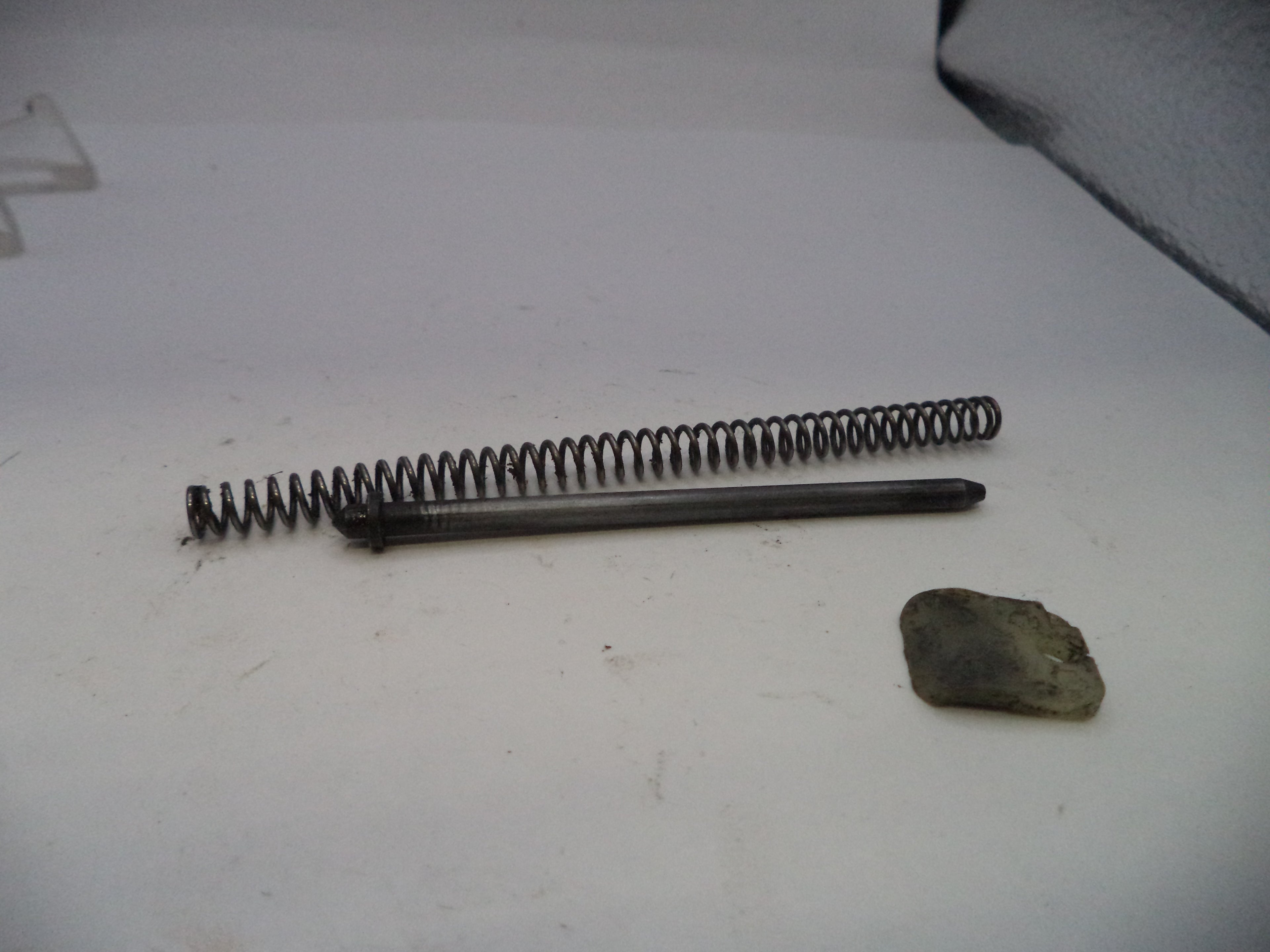 Metal spring and cylindrical object on a white surface with a small rock.