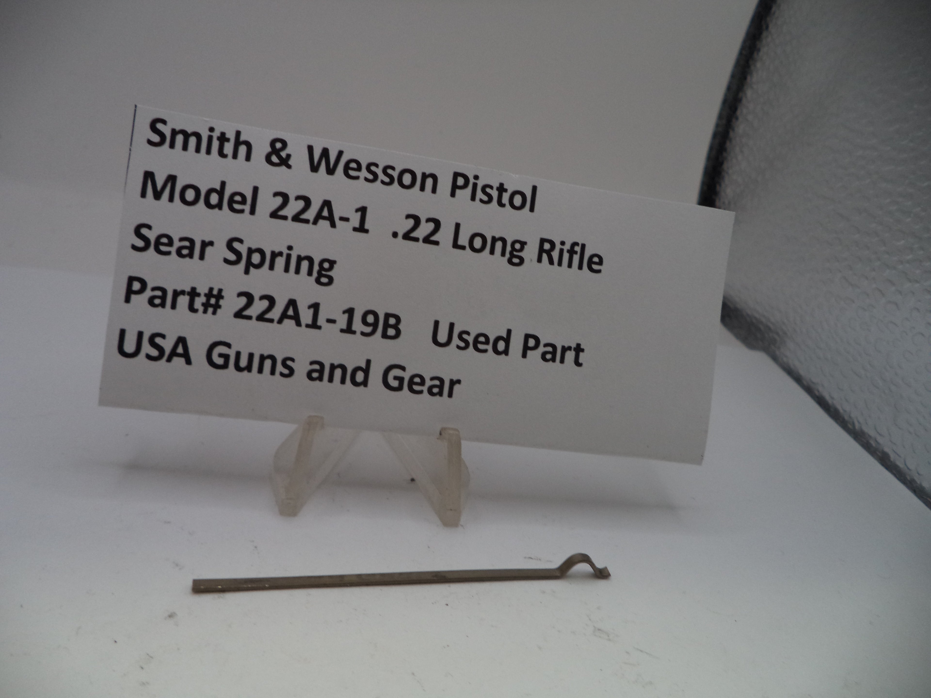 Small metal part of a Smith & Wesson pistol with a label on a white background