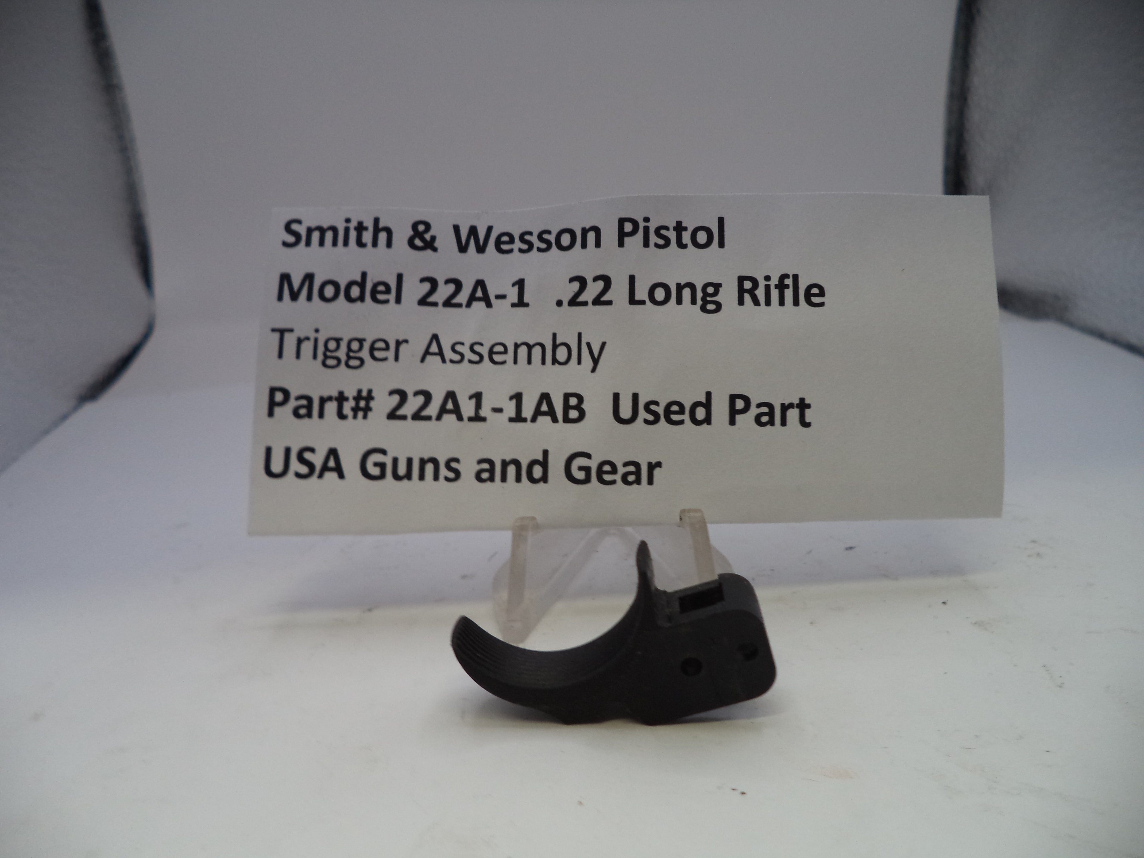 Smith & Wesson pistol trigger assembly on a stand with a label