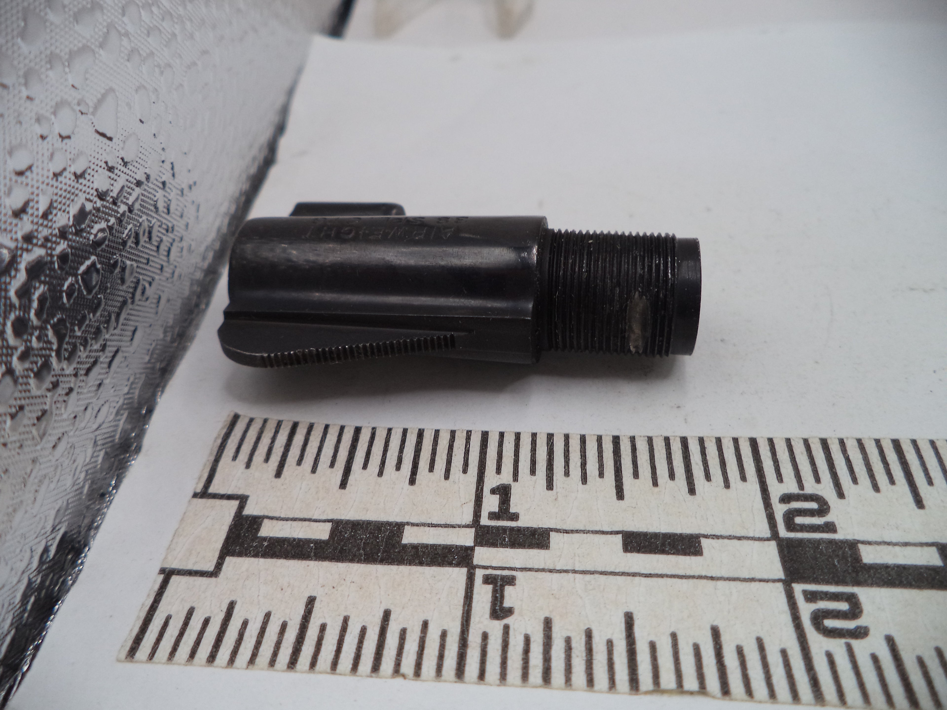 Black cylindrical object on a white surface with a ruler for scale.