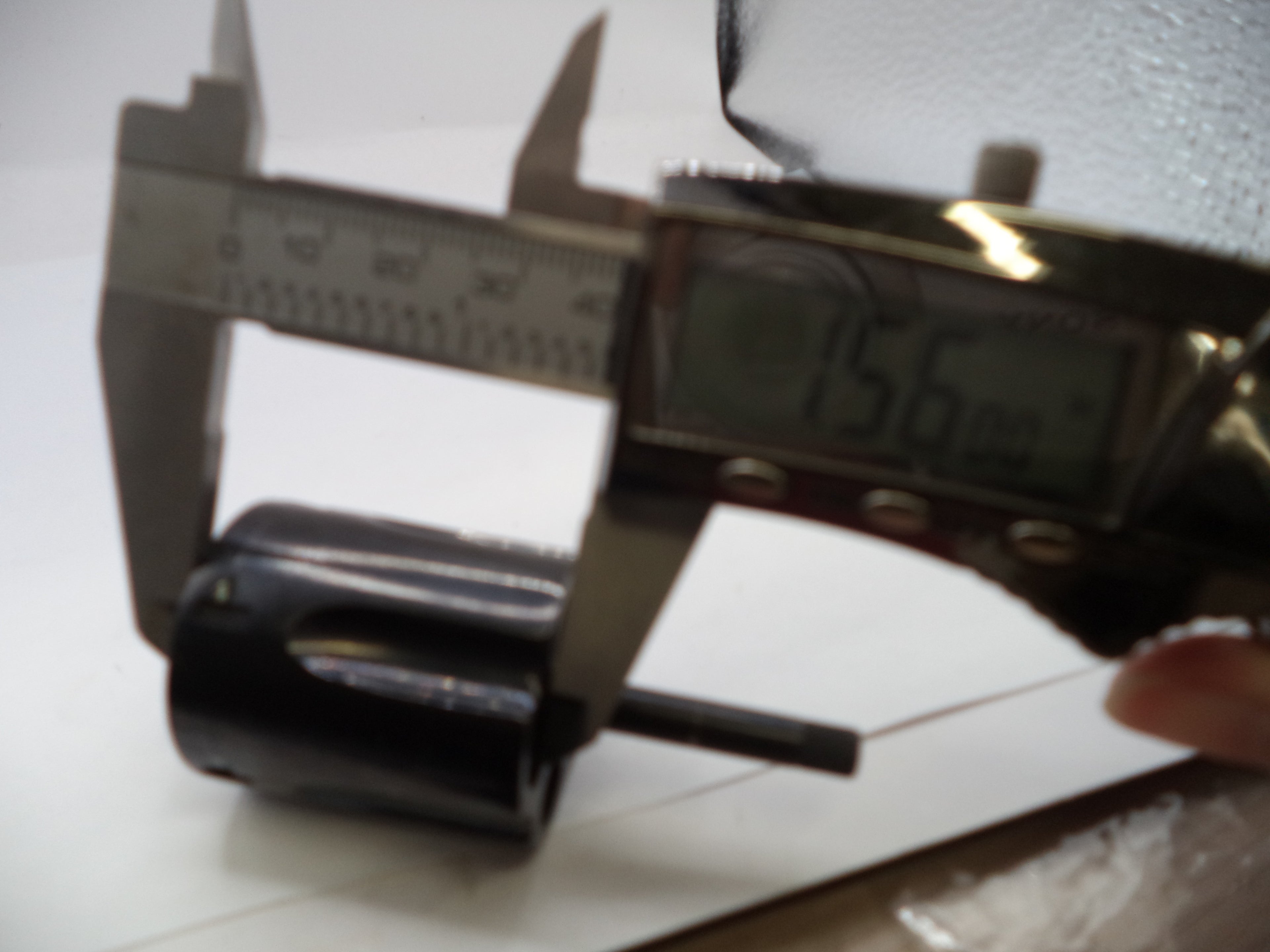 Digital caliper measuring a black cylindrical object on a white surface