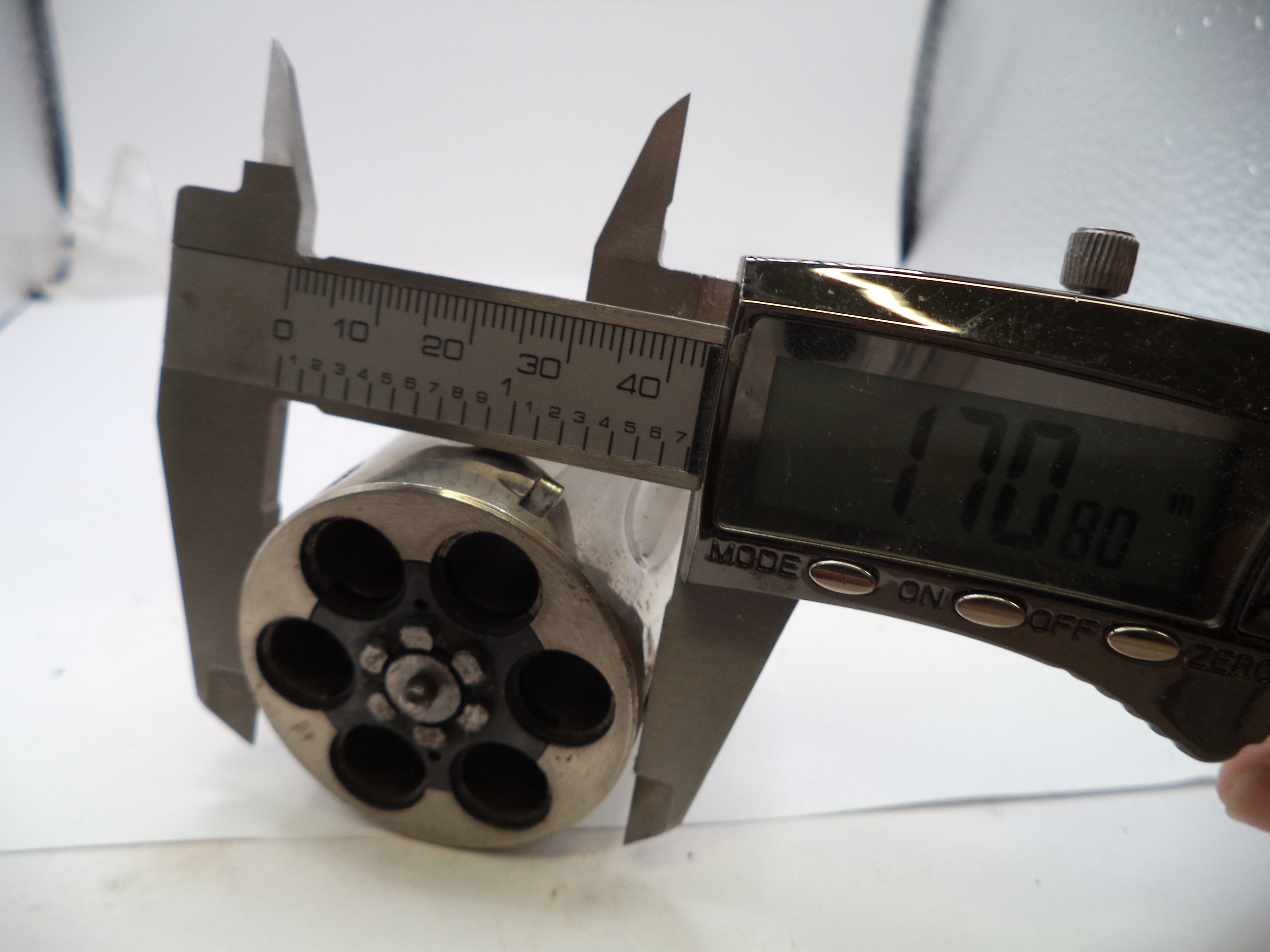 Metal cylindrical object with multiple holes being measured by a digital caliper on a white background