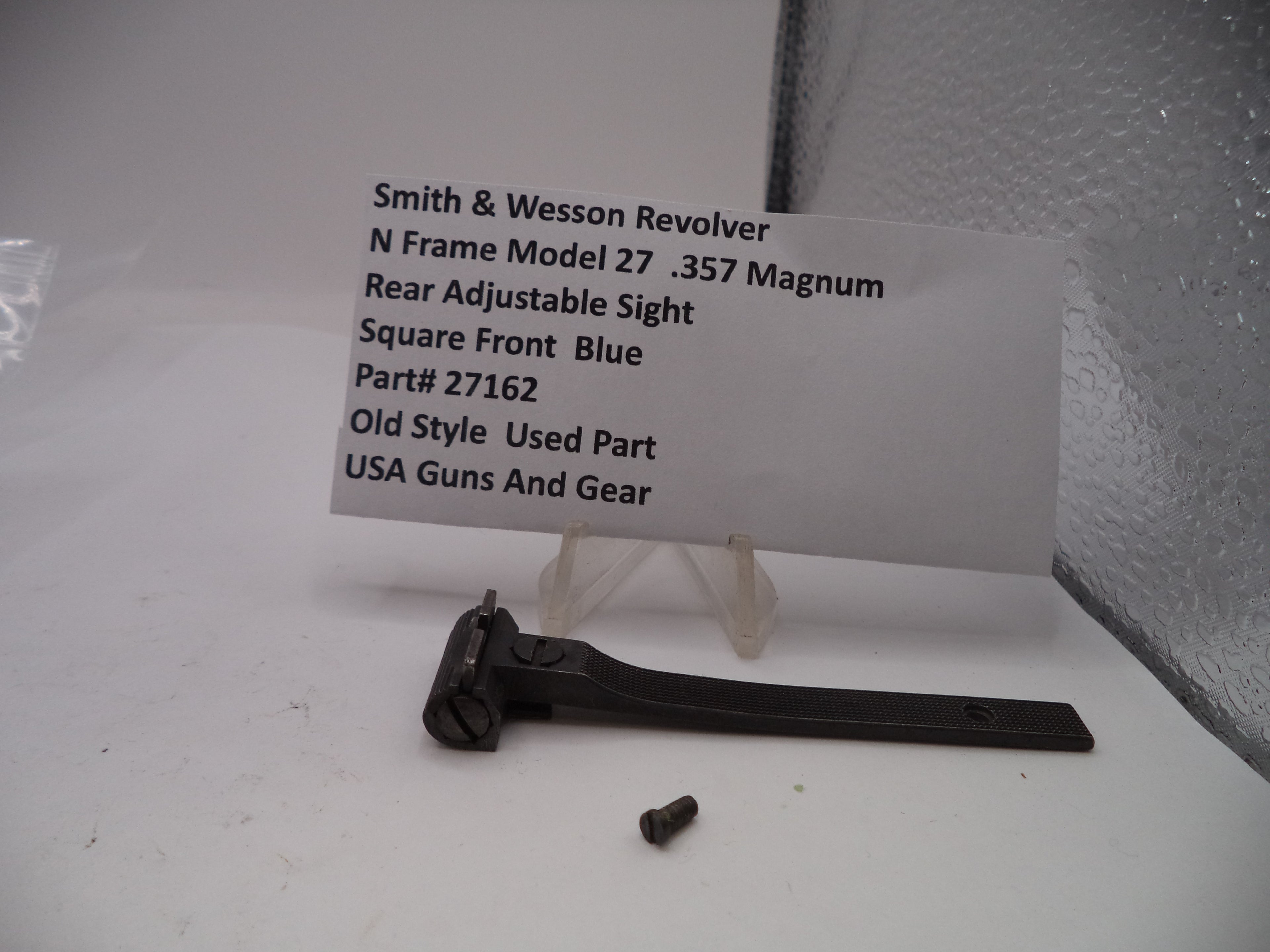 Smith & Wesson revolver rear adjustable sight on a white surface with a label.