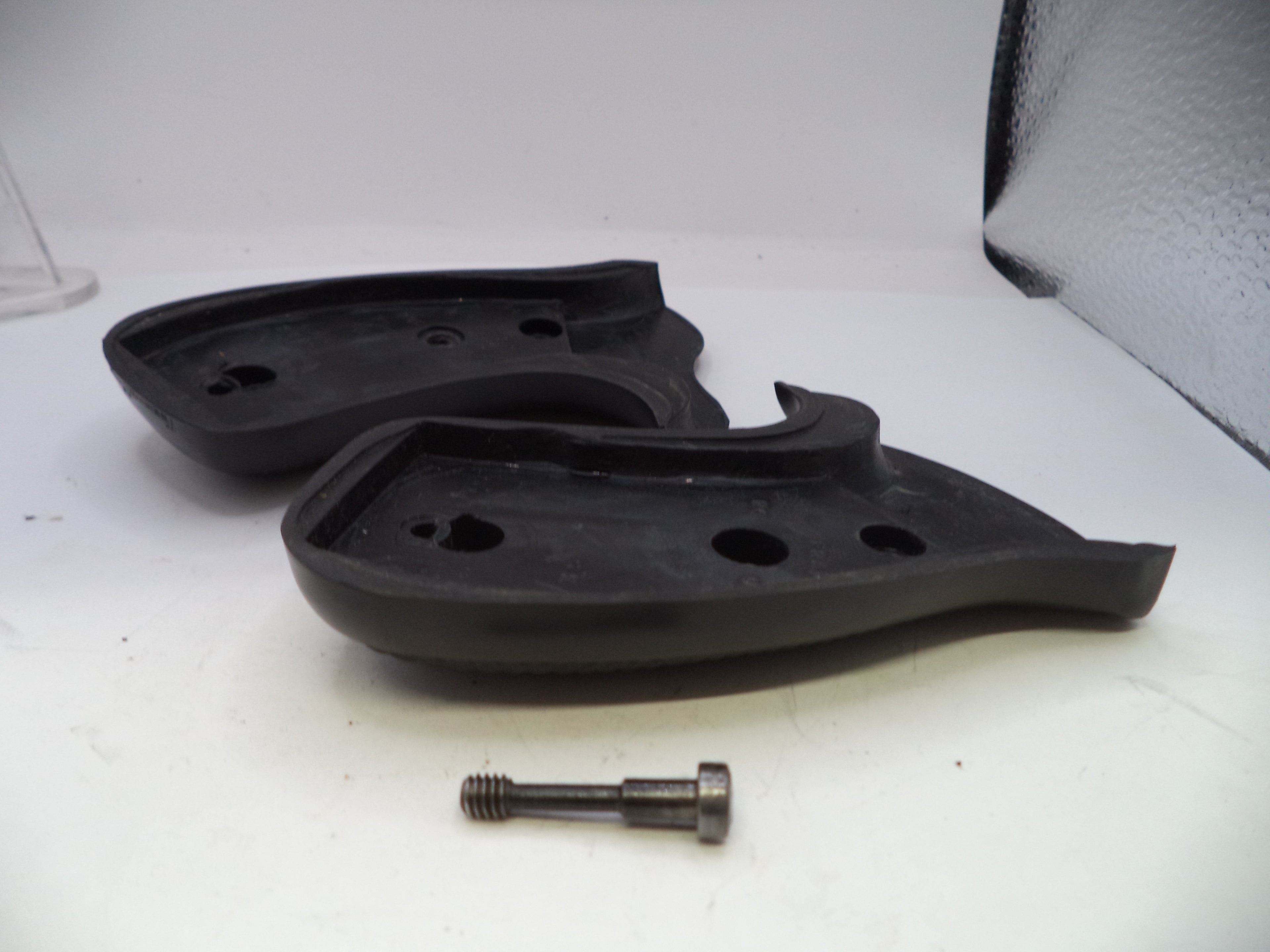 Two black rubber components with holes and a metal screw on a white surface.