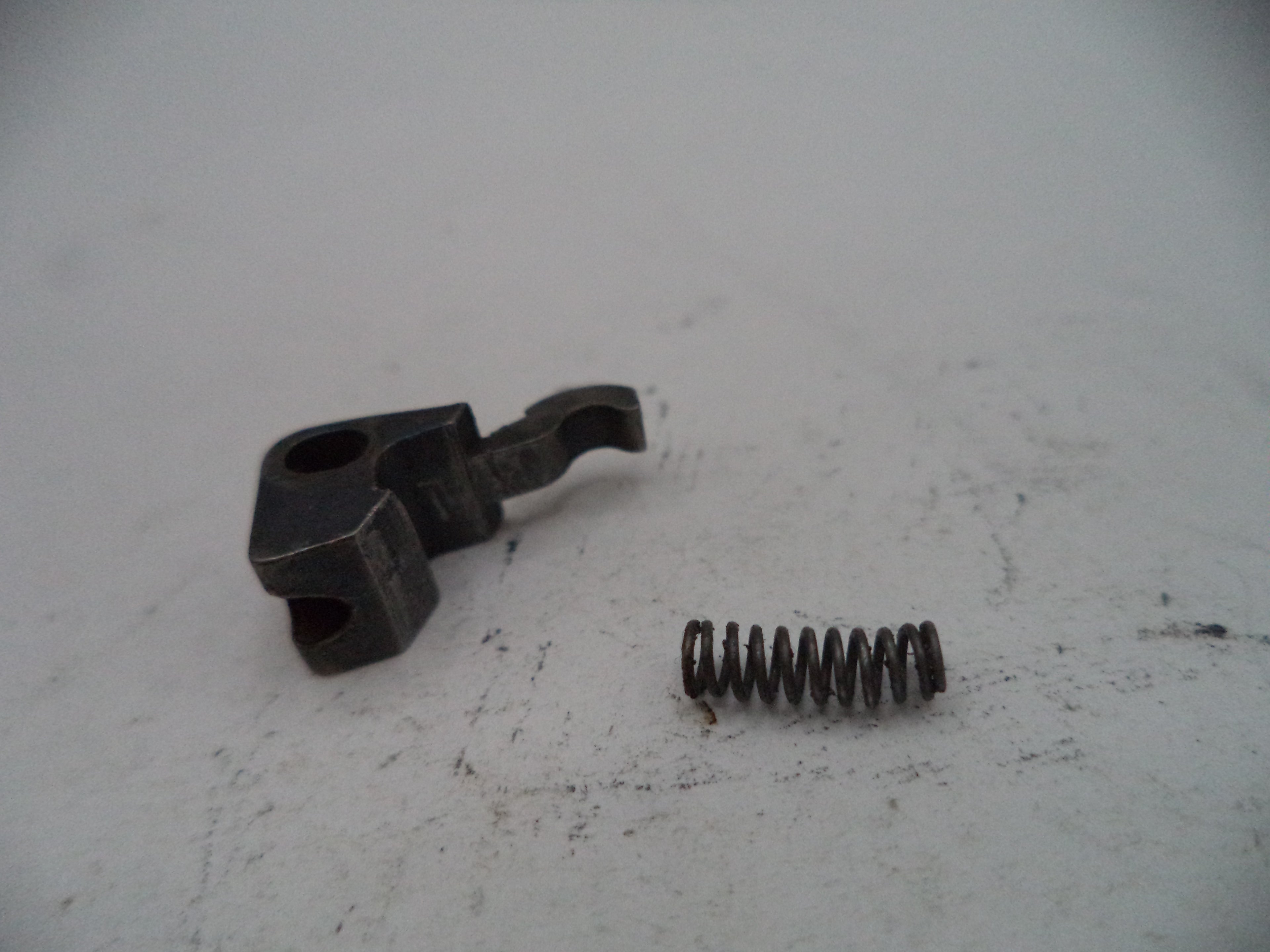 Mechanical parts including a black metal bracket and a coiled spring on a white surface.