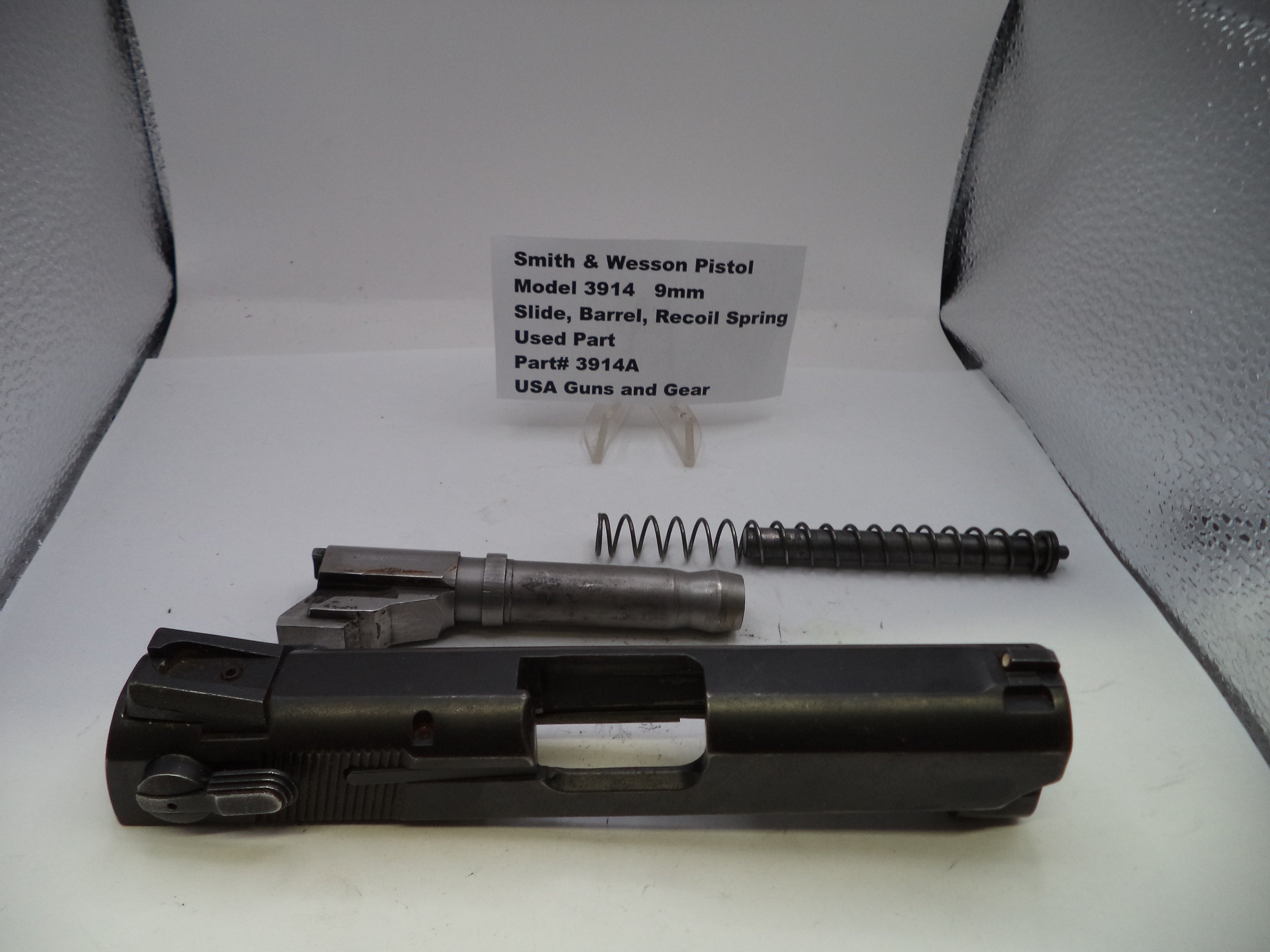 Smith & Wesson pistol parts including slide, barrel, and recoil spring on a white surface with a label.