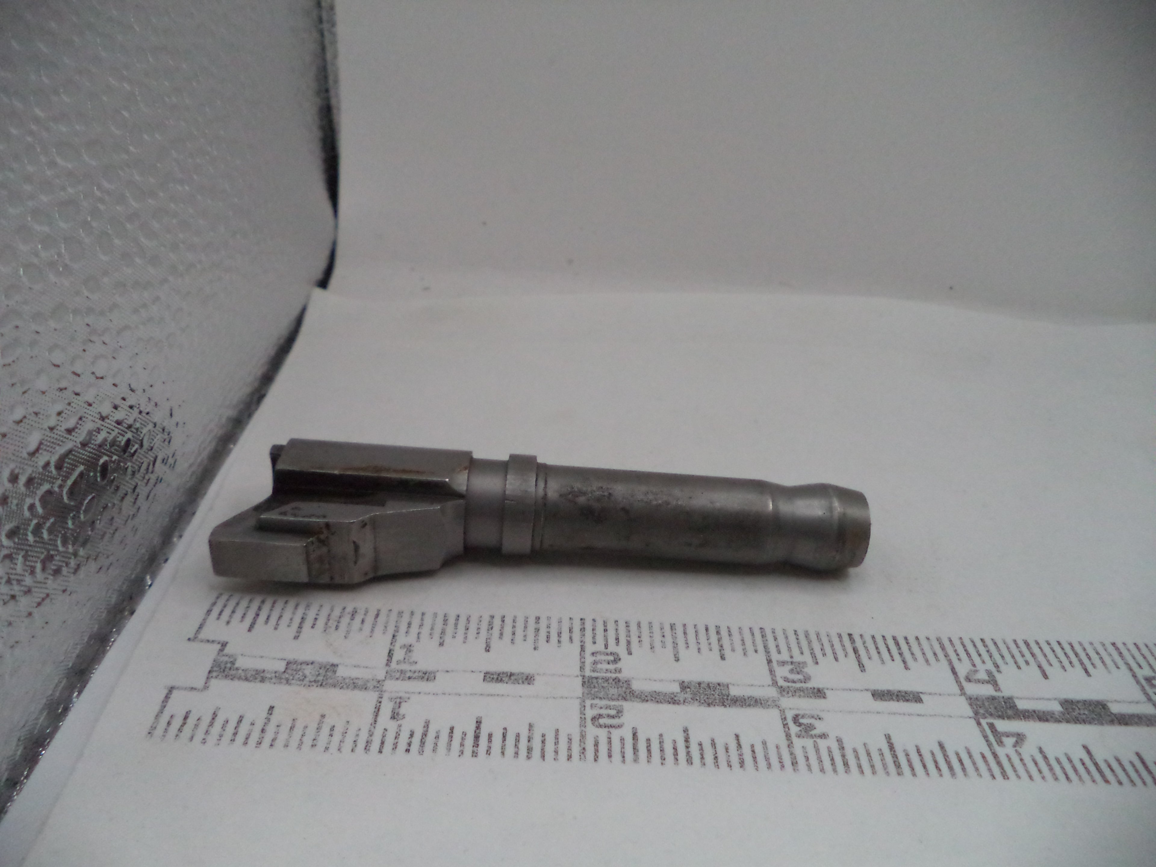 Metal component on a white surface with a ruler for scale