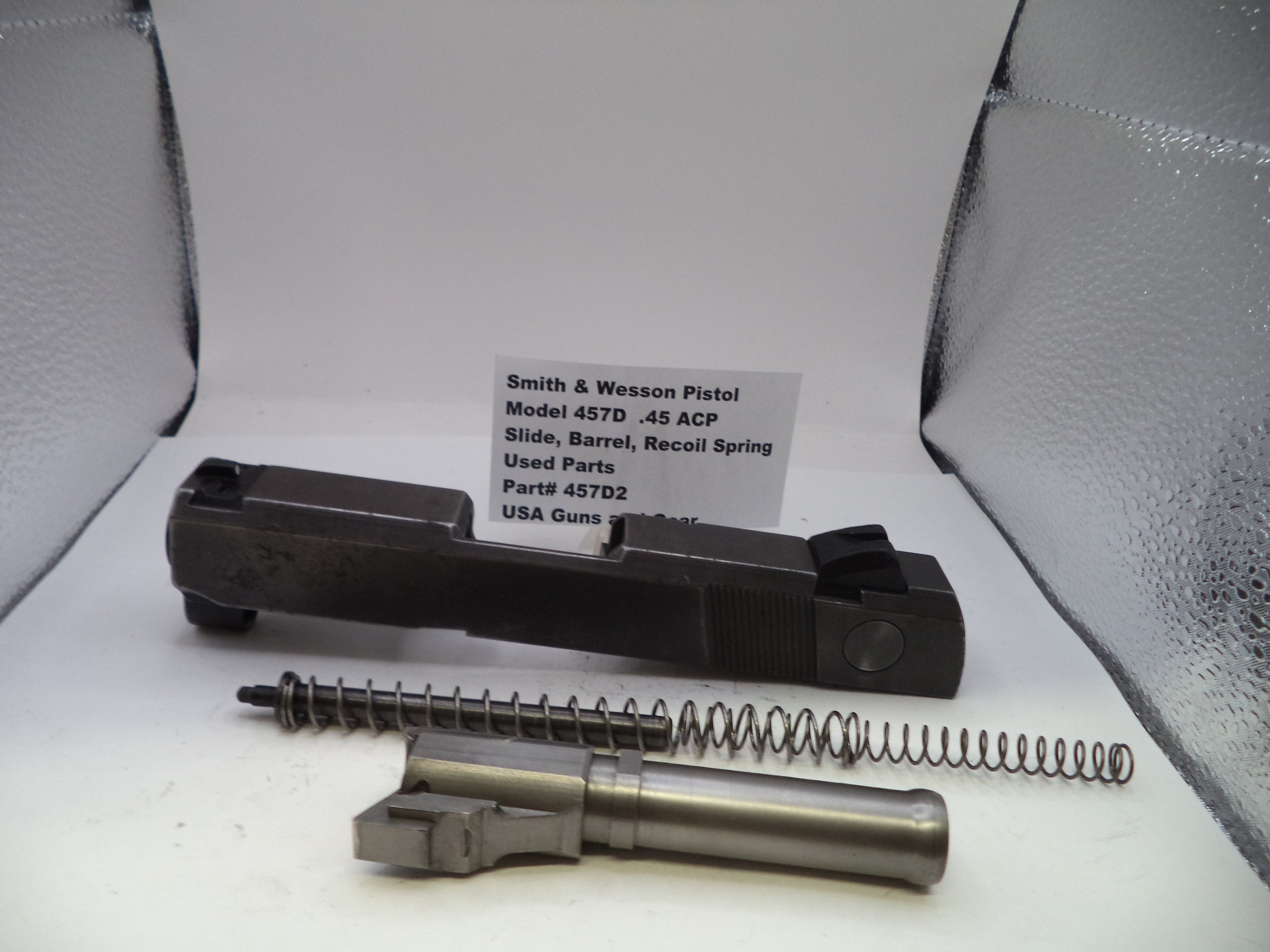 Smith & Wesson pistol parts including slide, barrel, and recoil spring on a white background with a label.