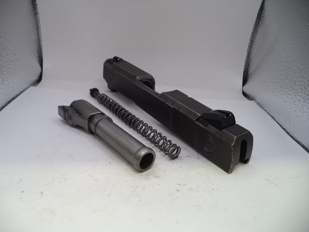 Gun components including a barrel, slide, and spring on a white surface.