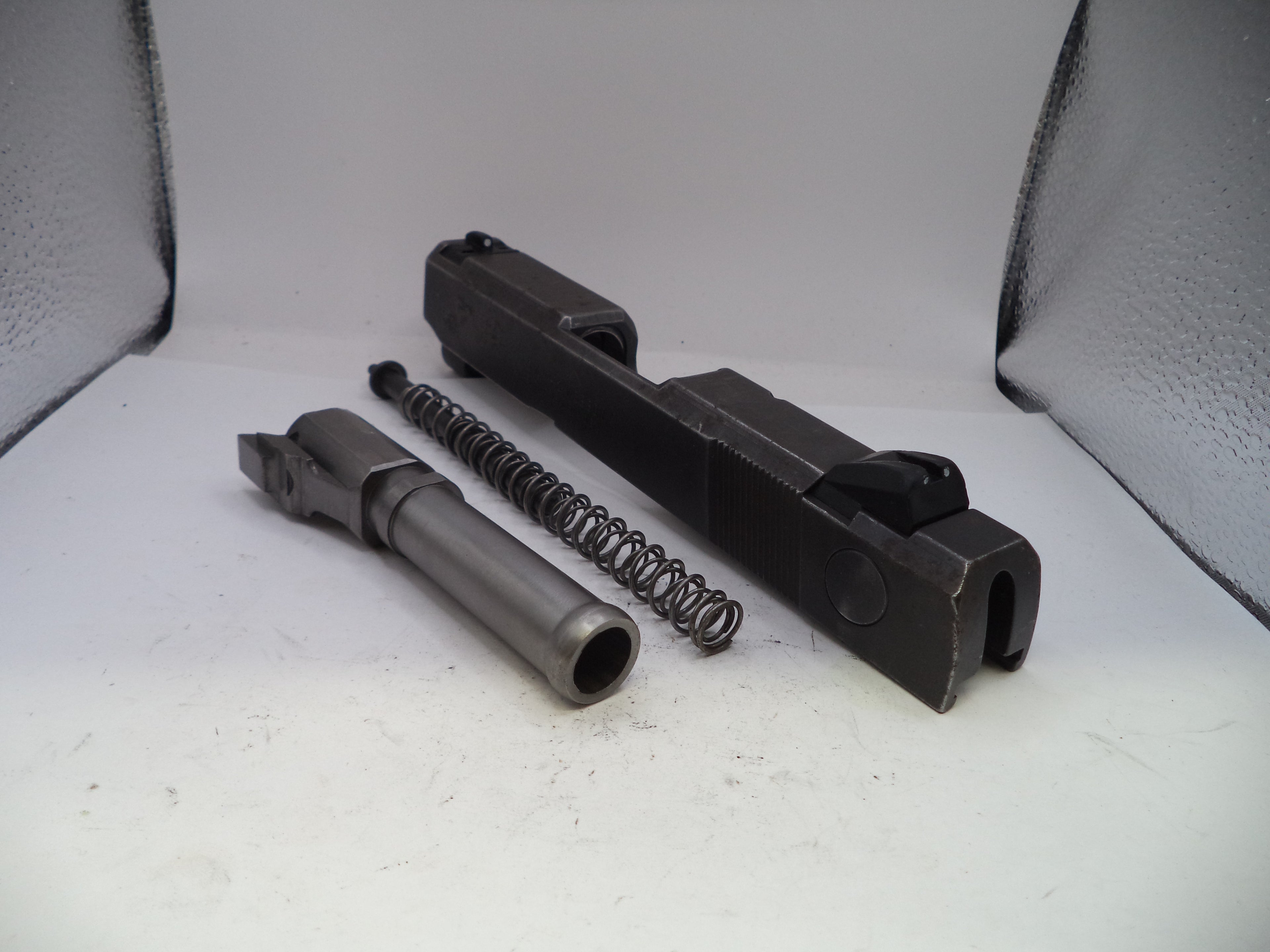 Gun components including a barrel, slide, and spring on a white surface.