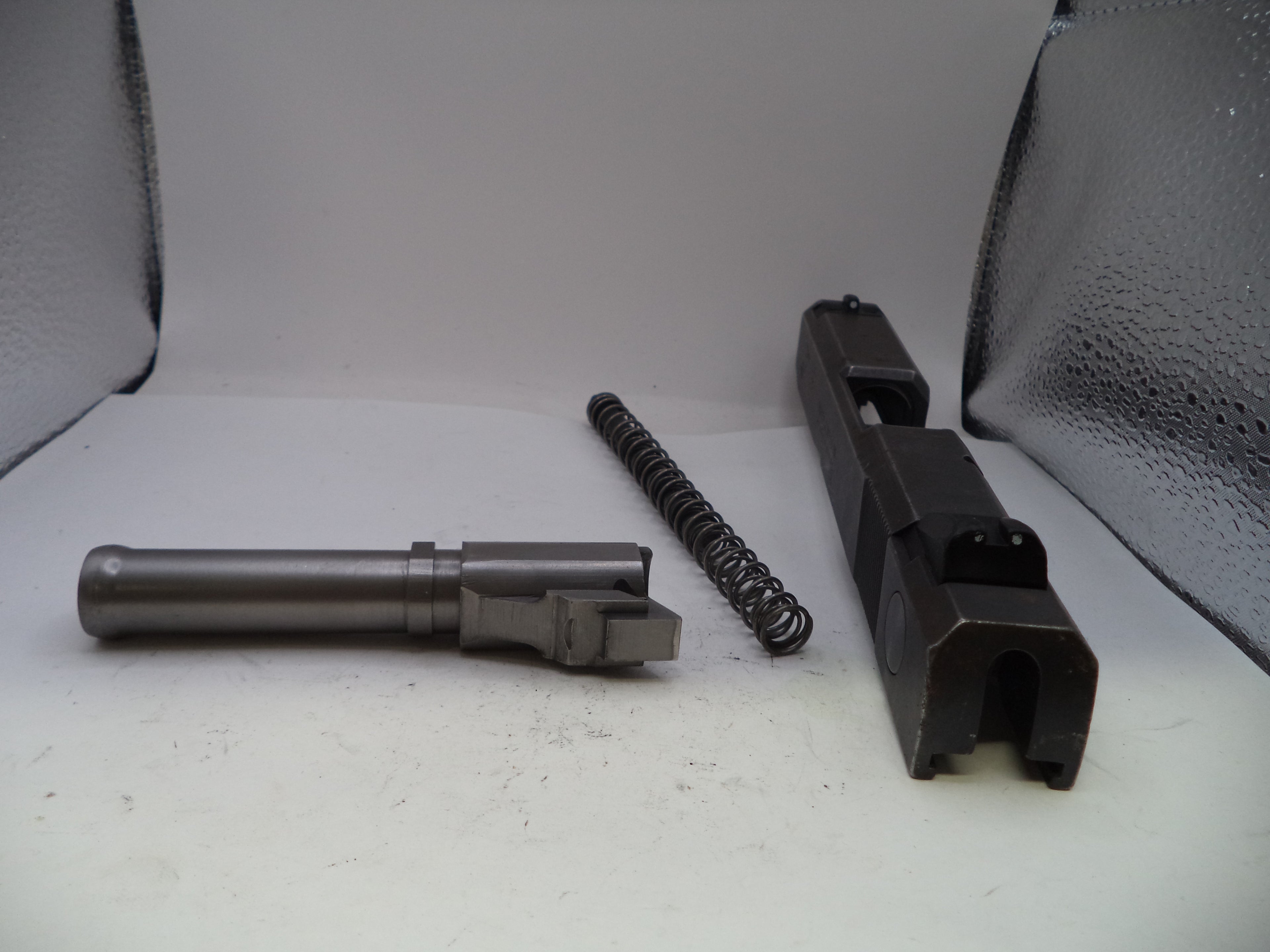 Three gun components on a white surface with a gray textured background