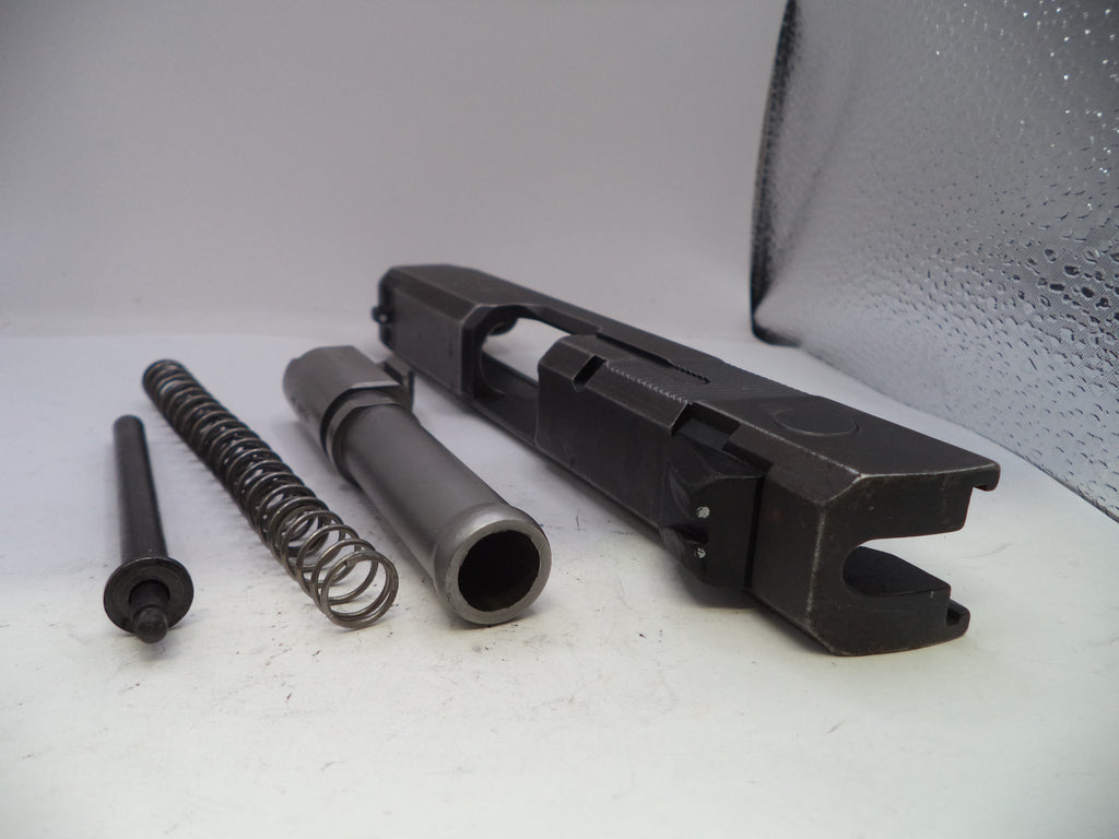 Black metal gun slide, spring, and other components on a white surface with a gray background.