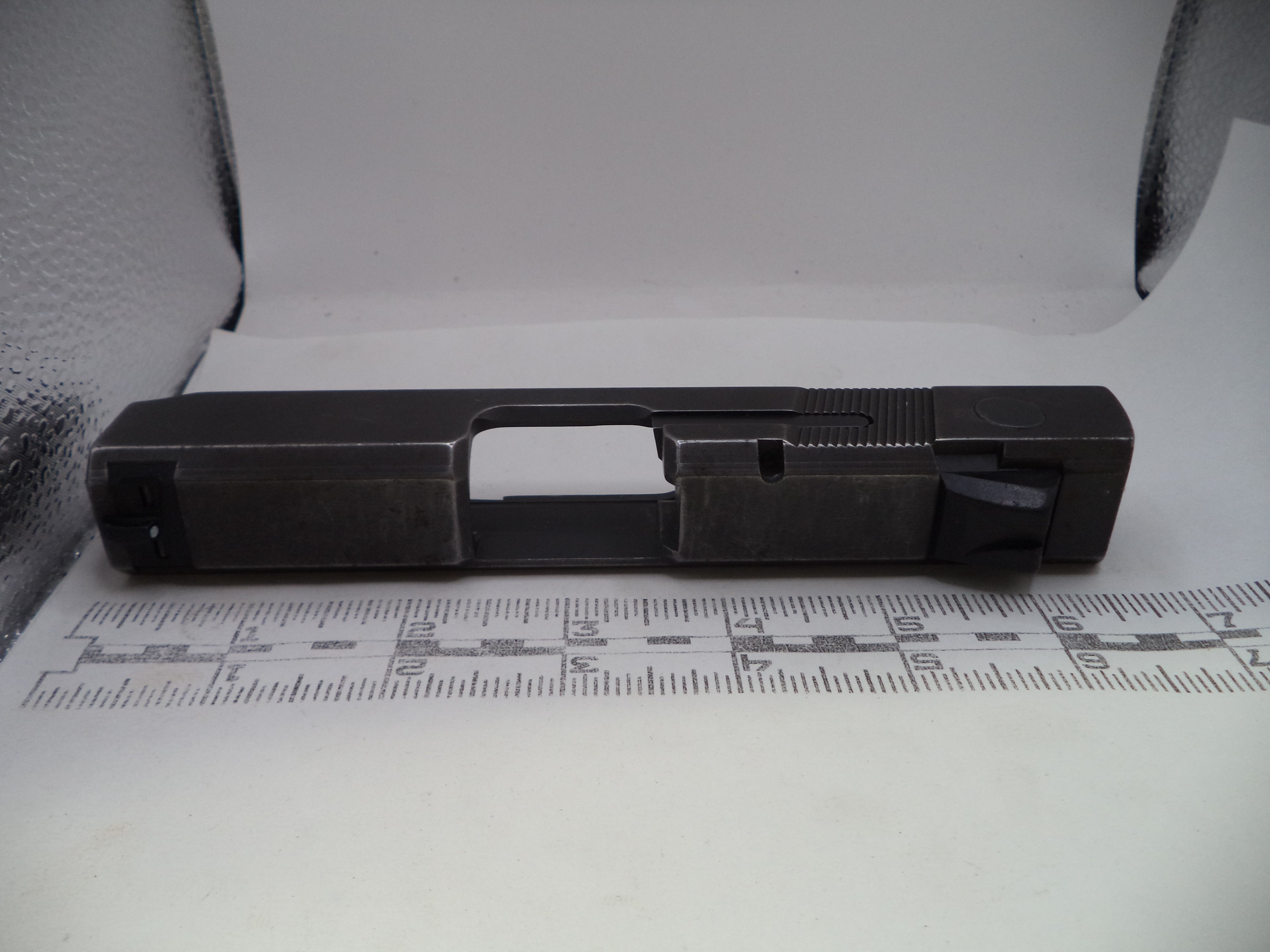 Black metal component on a white surface with measurement scale