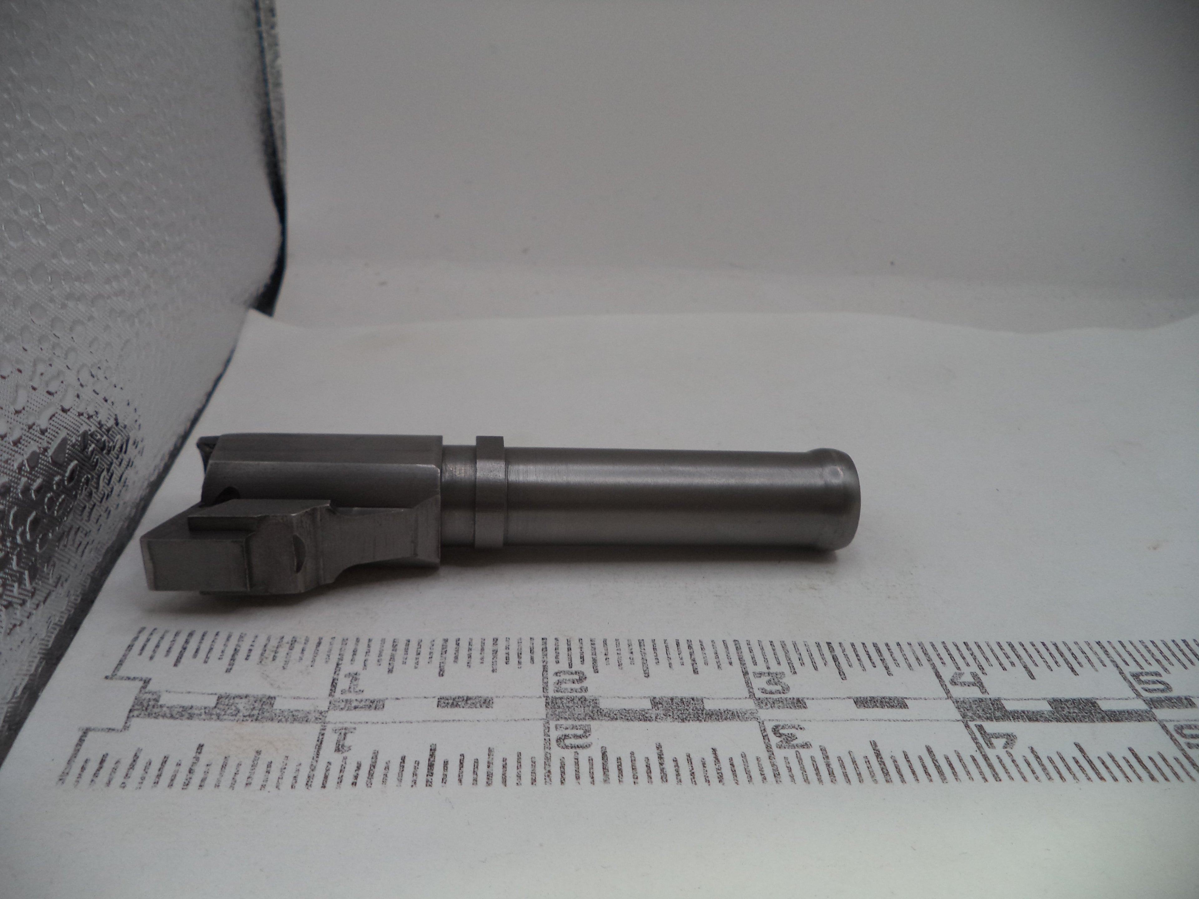 Metal gun barrel on a white surface with measurement scale