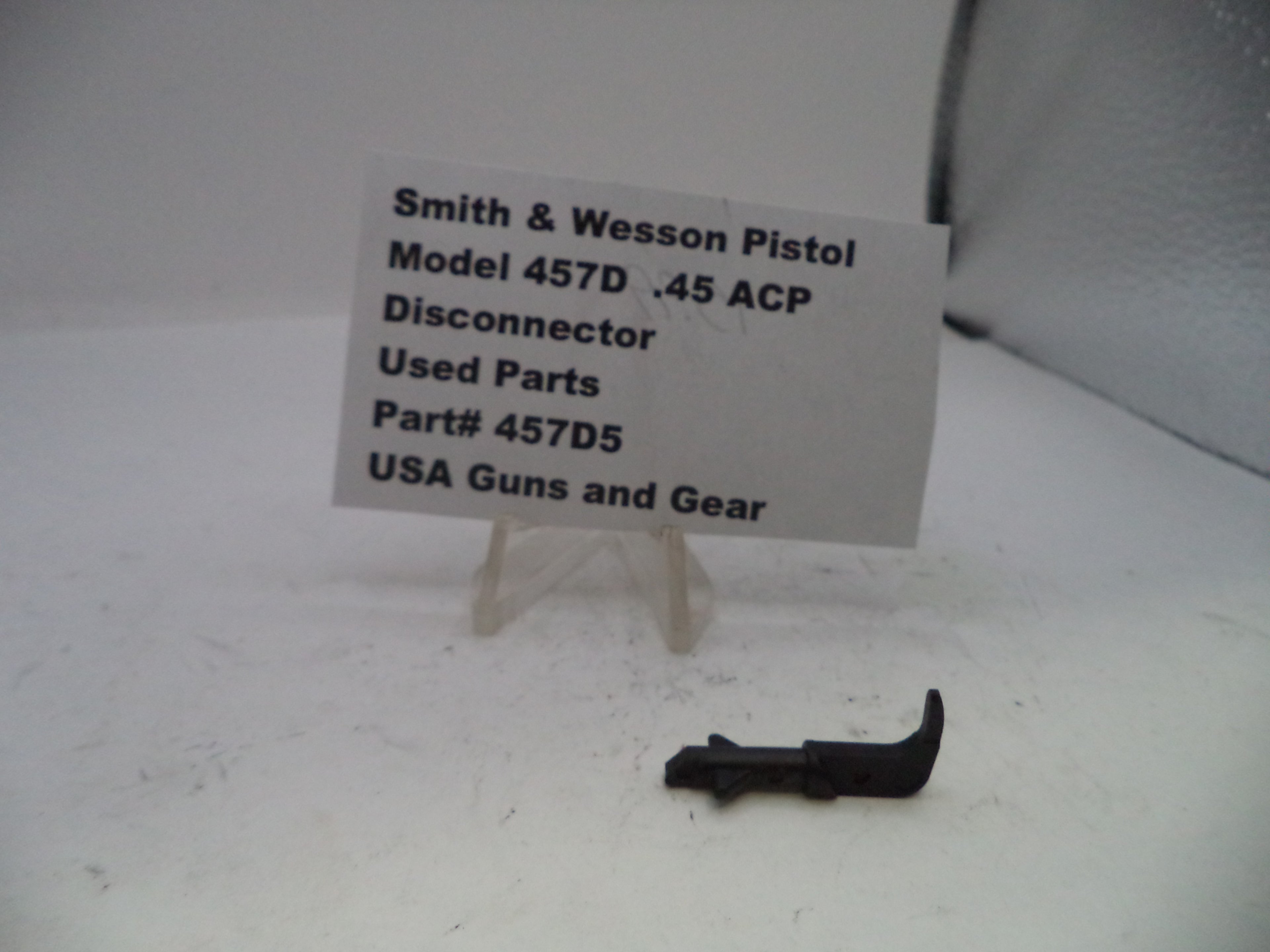 Used parts of a Smith & Wesson Pistol Model 457D .45 ACP Disconnector on a white background with a label.