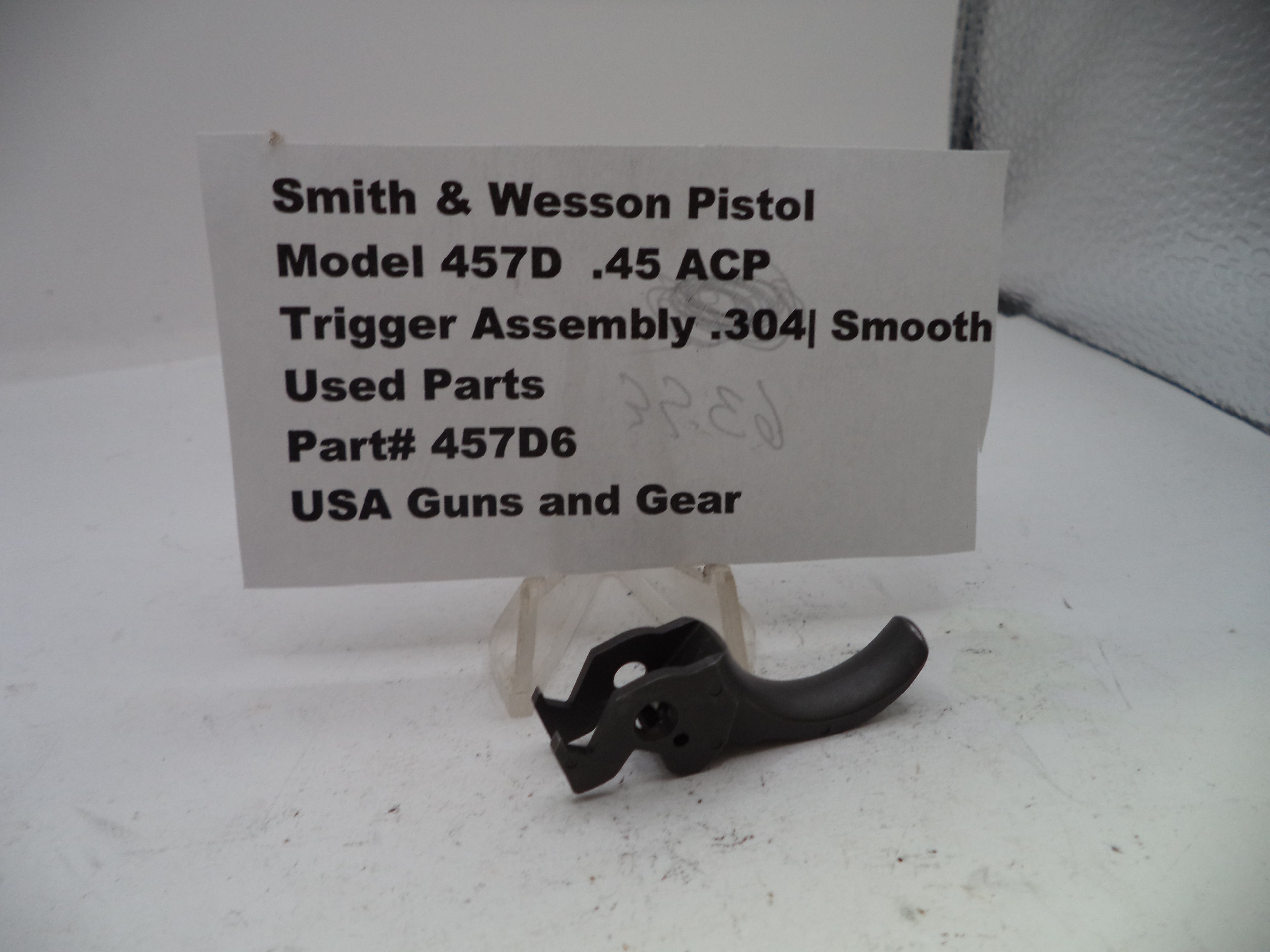 Smith & Wesson pistol trigger assembly on a white background with a label.