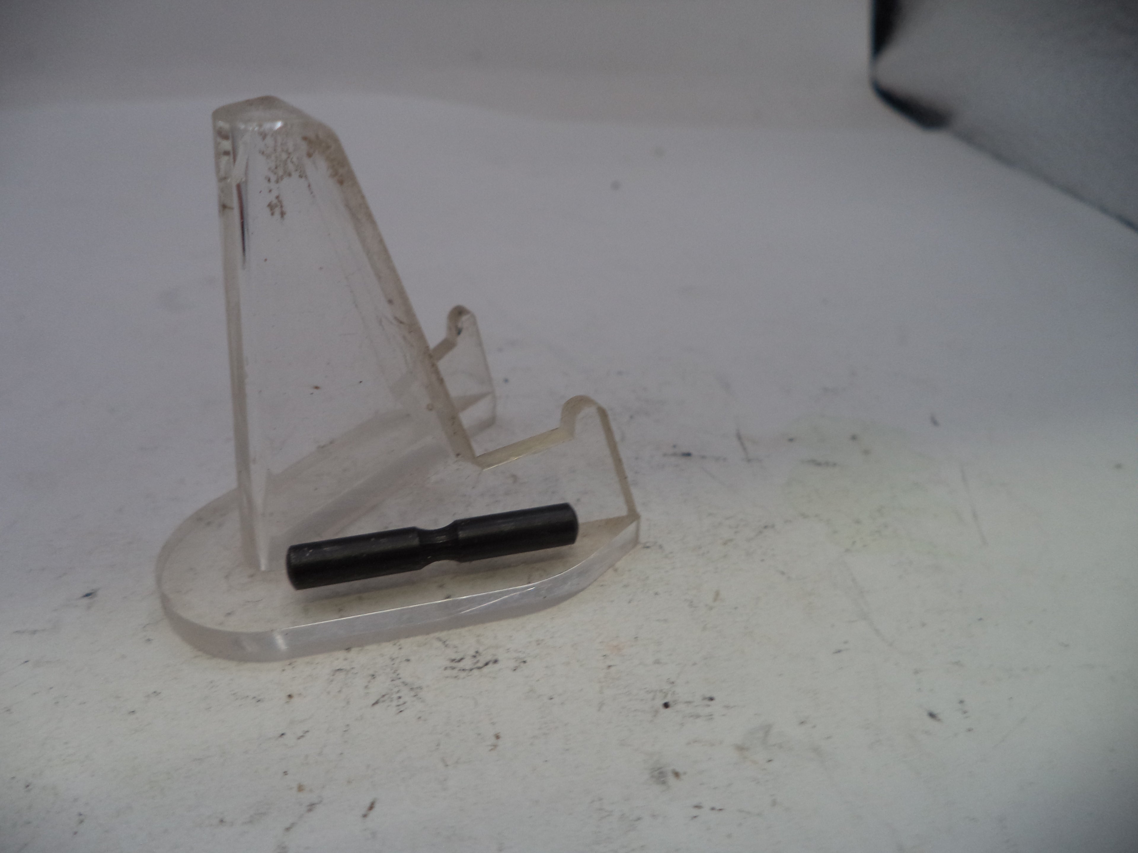 Clear plastic stand with a black cylindrical object on a white surface